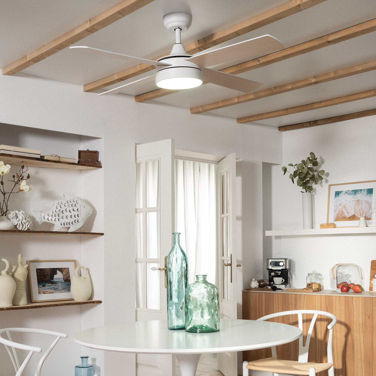 Una stanza luminosa con un ventilatore a soffitto, un tavolo rotondo e oggetti decorativi su mensole e sul tavolo.