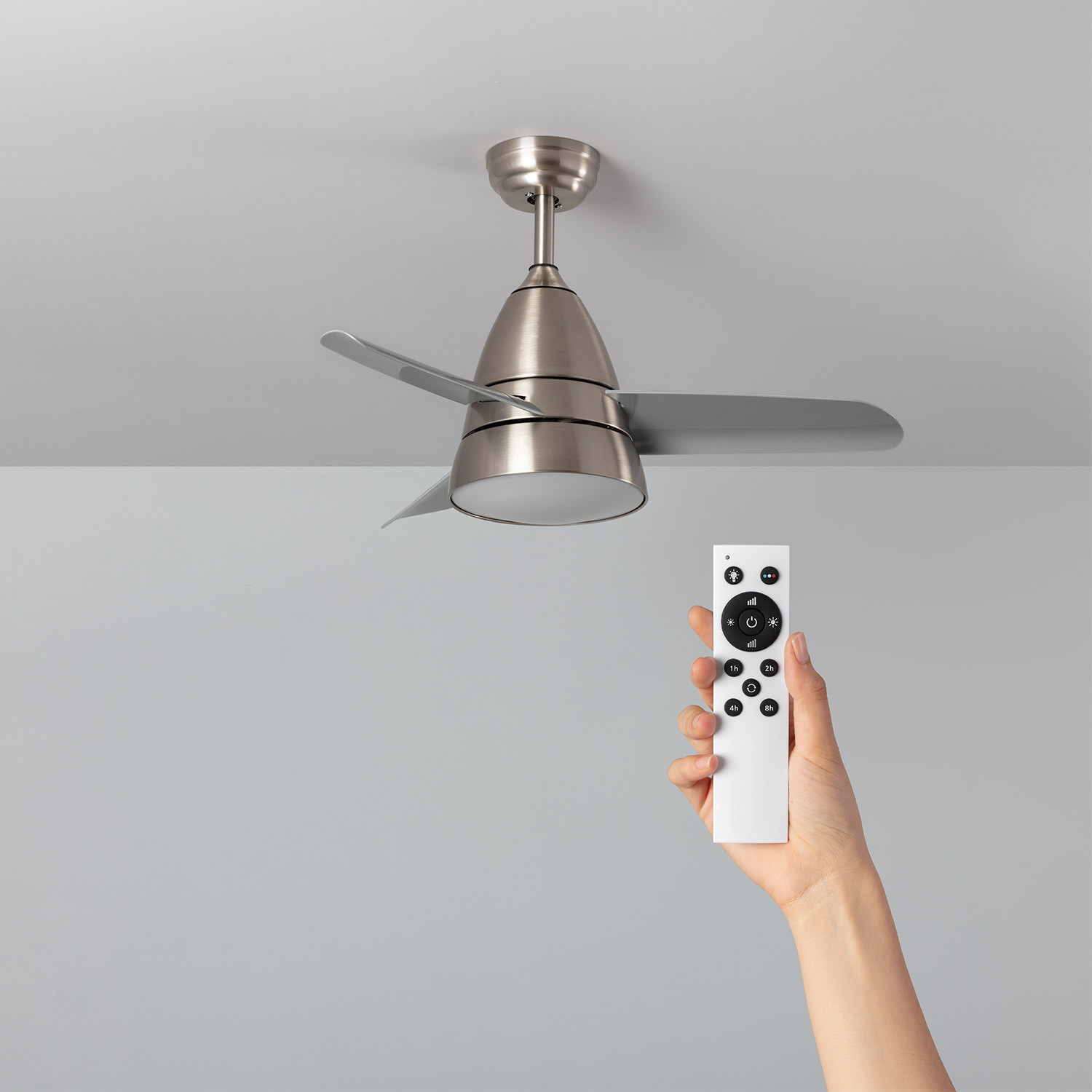 Una mano che tiene un telecomando bianco, che punta verso un ventilatore a soffitto.