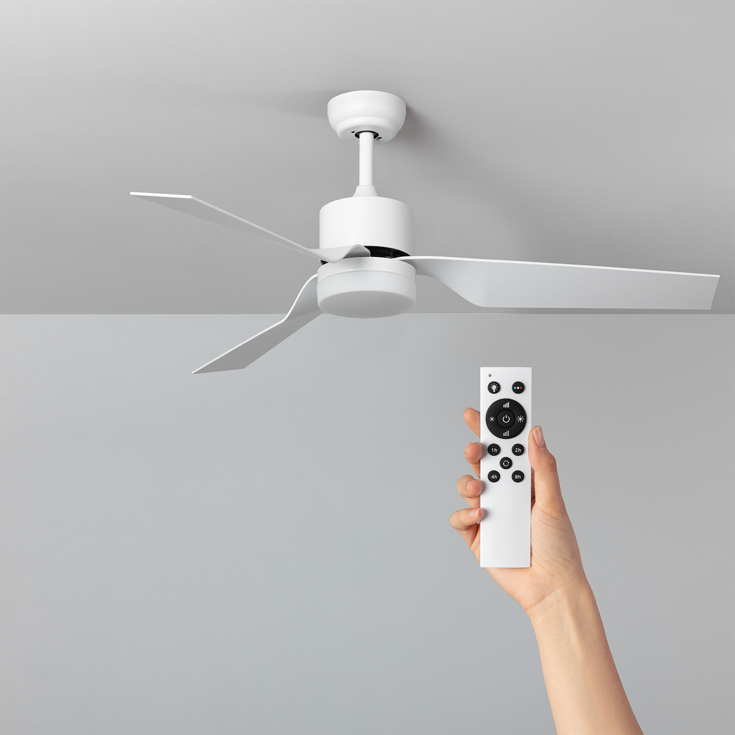 Ventilatore da soffitto bianco con telecomando in mano. Soffitto grigio sullo sfondo.