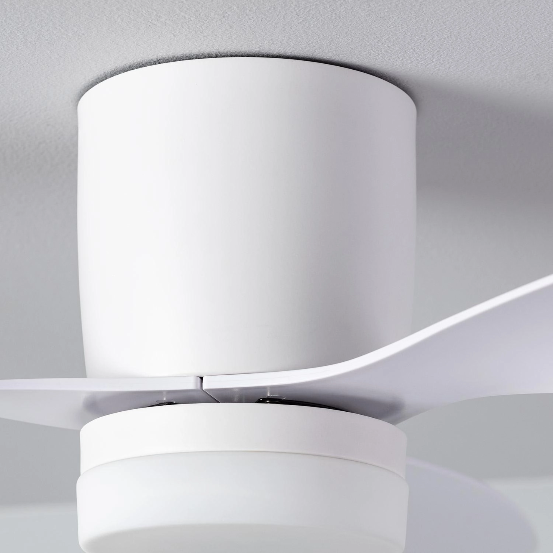 Primo piano di un ventilatore da soffitto bianco con tre pale. Il soffitto è bianco.
