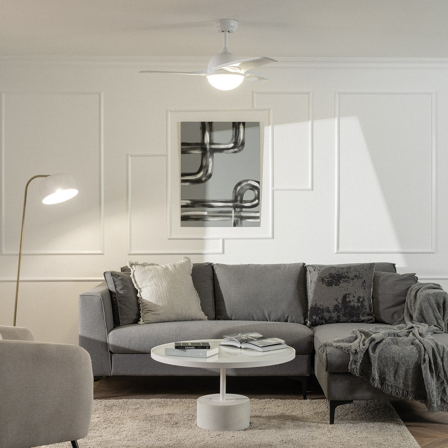 Un soggiorno presenta un divano grigio, un plaid, cuscini, opere d'arte e un ventilatore a soffitto bianco.