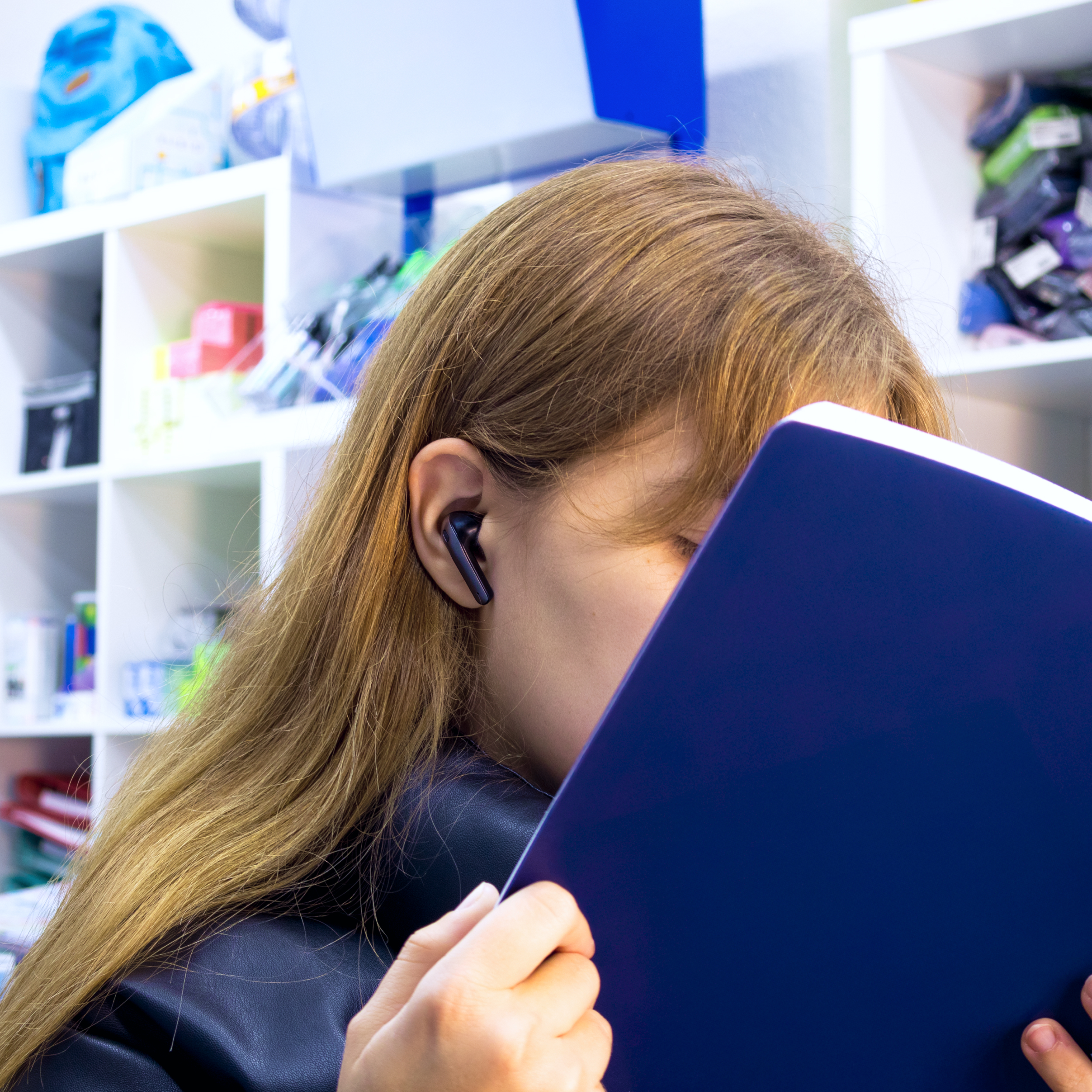 Una donna con un auricolare nell'orecchio, legge un libro, in un negozio.