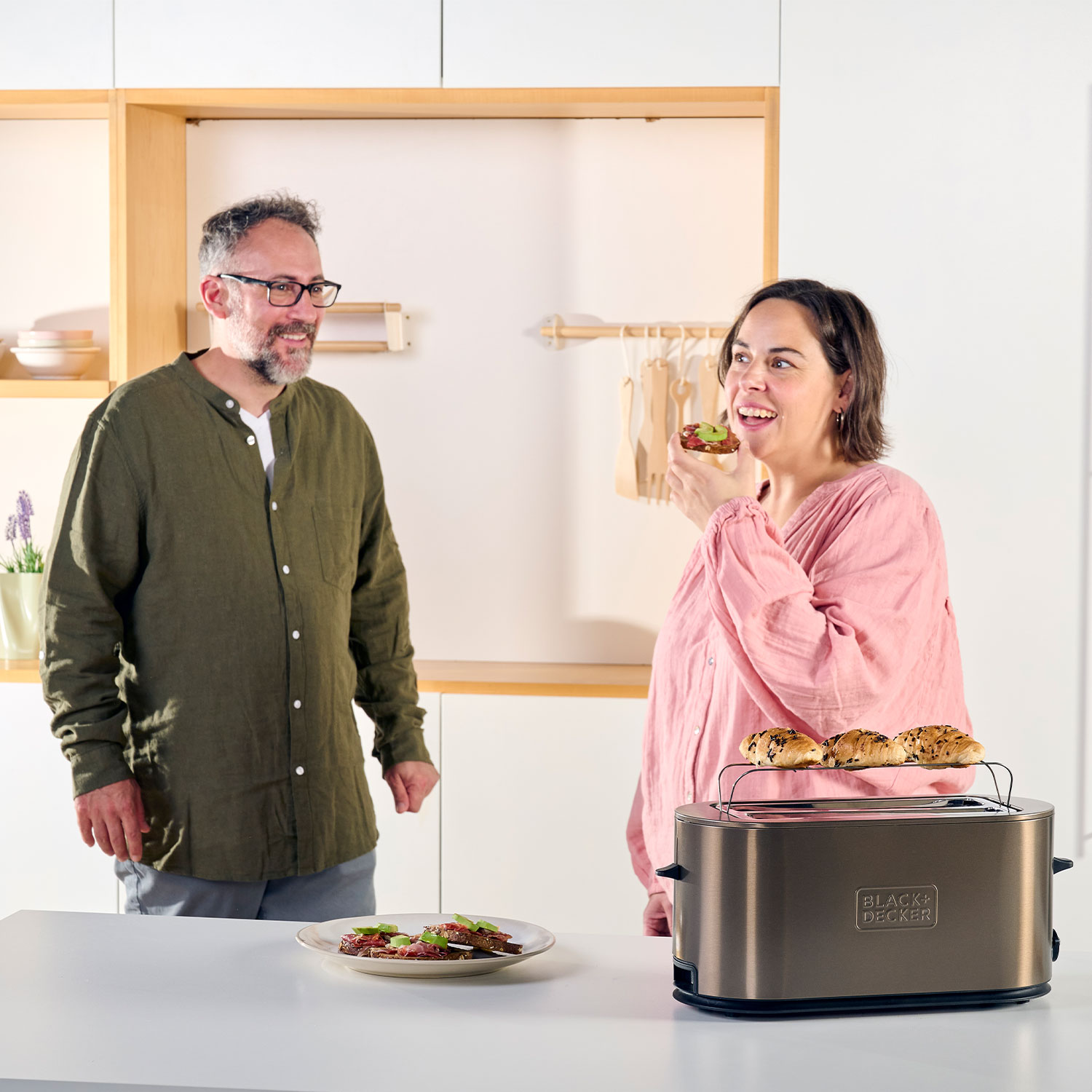 Ein Paar in der Küche: Der Mann beobachtet, wie die Frau Toast aus einem Black & Decker Toaster isst.