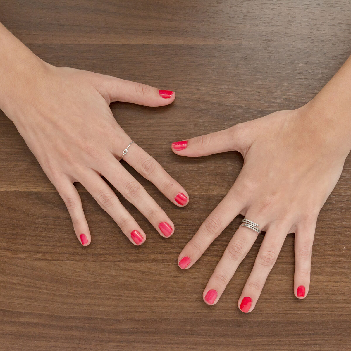 Manos con esmalte de uñas rojo sobre una superficie de madera. Una mano tiene un anillo.