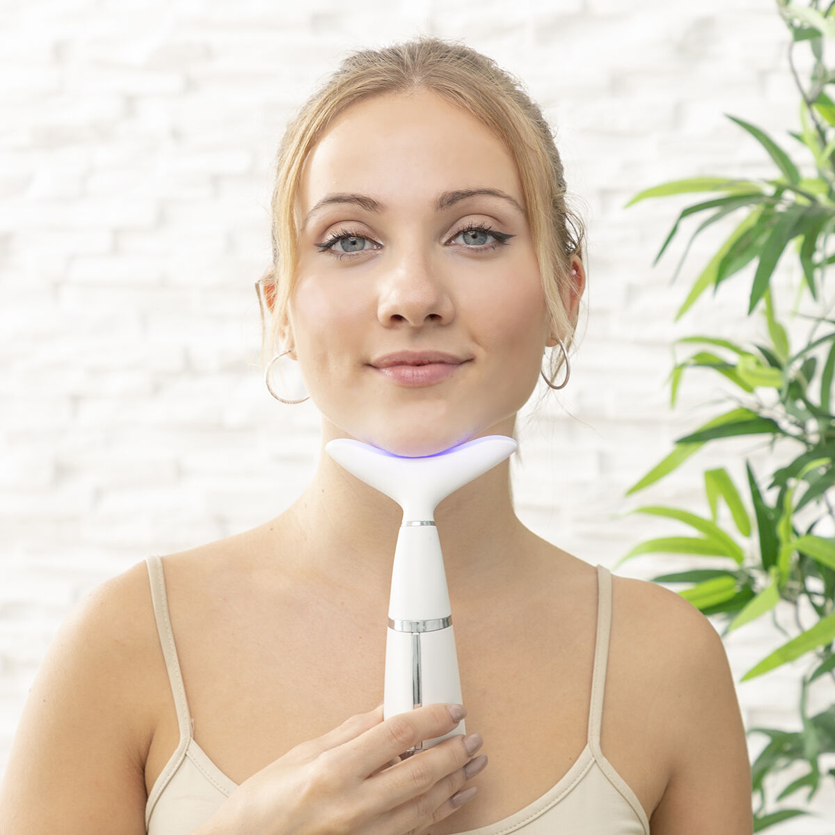 Blonde Frau mit einem Gesichtsmassagegerät. Sie schaut in die Kamera.