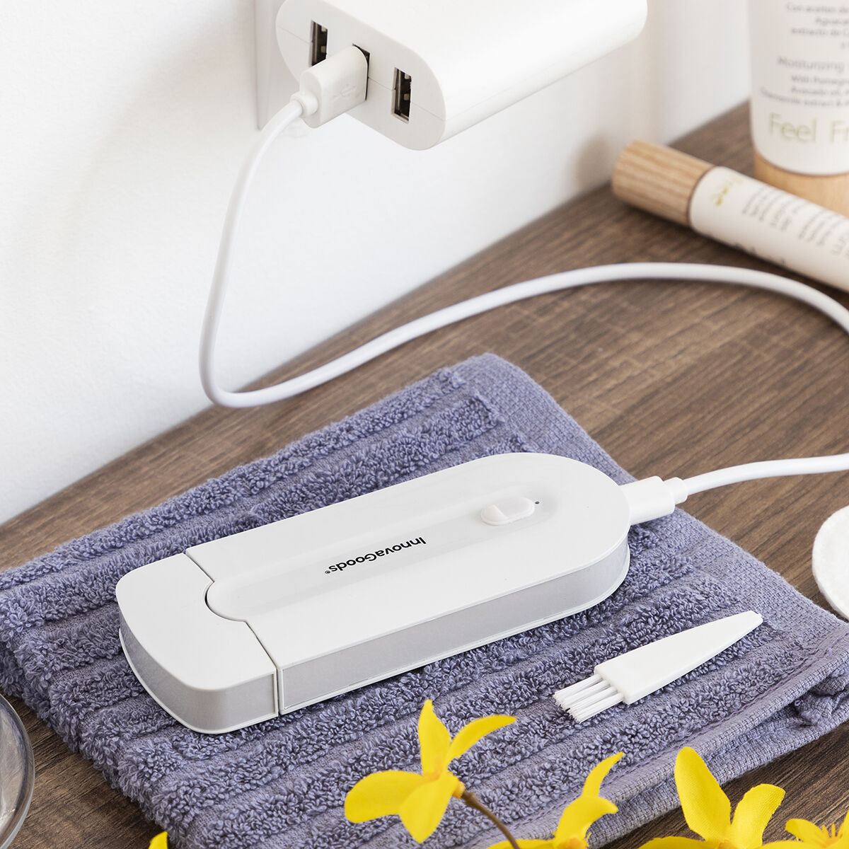 Weißes Gerät, das in einem USB-Anschluss geladen wird, neben einer Bürste und einem Handtuch.