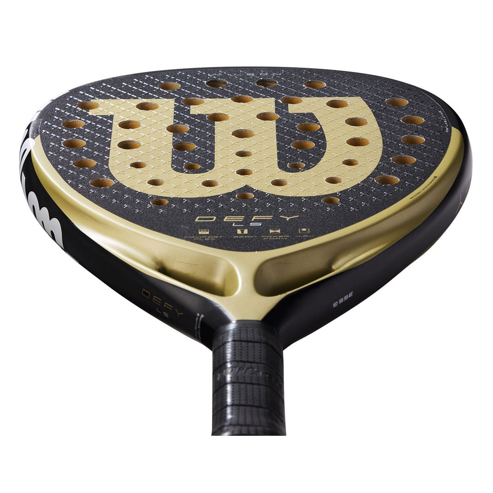 Primer plano de una pala de pádel Wilson negra y dorada. El logo 'W' es visible, junto con 'DEFY'.