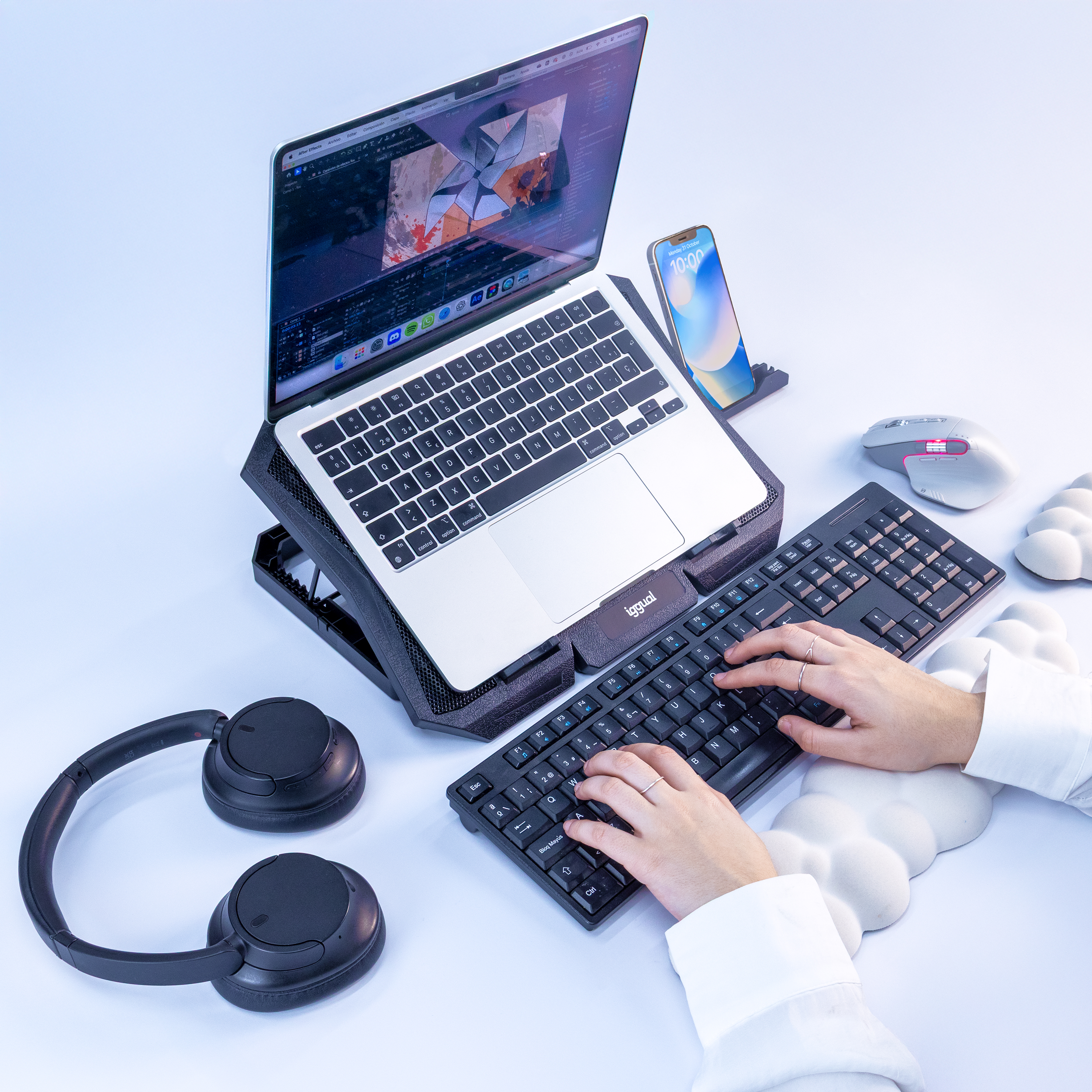 Osoba korzystająca z laptopa, klawiatury i myszy z telefonem na stojaku. Obecne są również słuchawki i podkładka pod mysz.