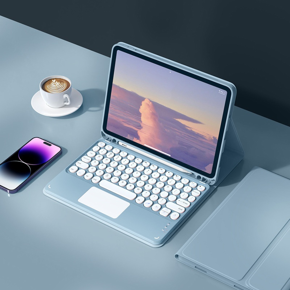 Een laptop met een toetsenbordhoes, een smartphone en een kopje koffie op een bureau.