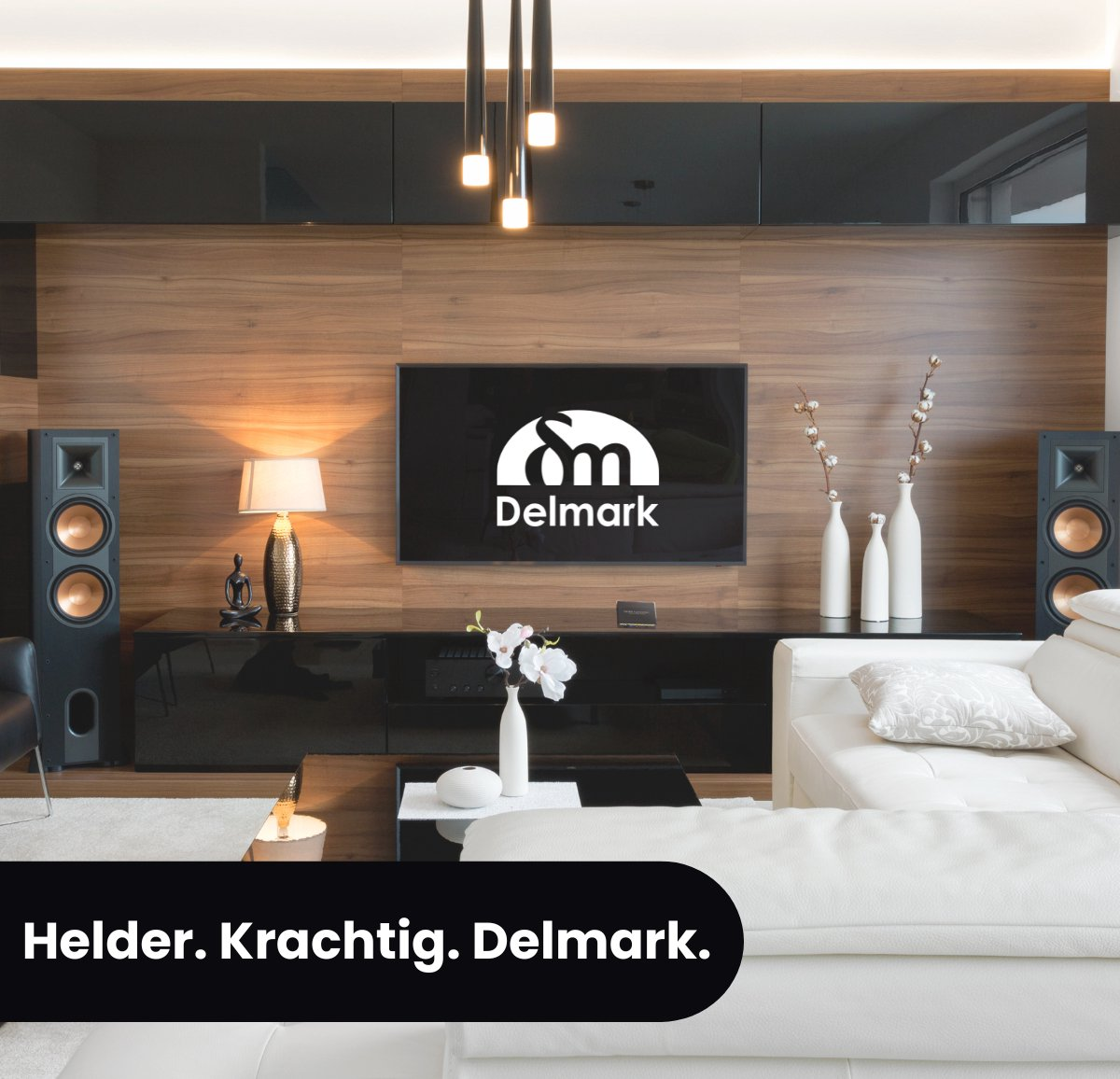 Woonkamer met een witte bank, zwarte kasten, tv, speakers, bloemen en Delmark logo.
