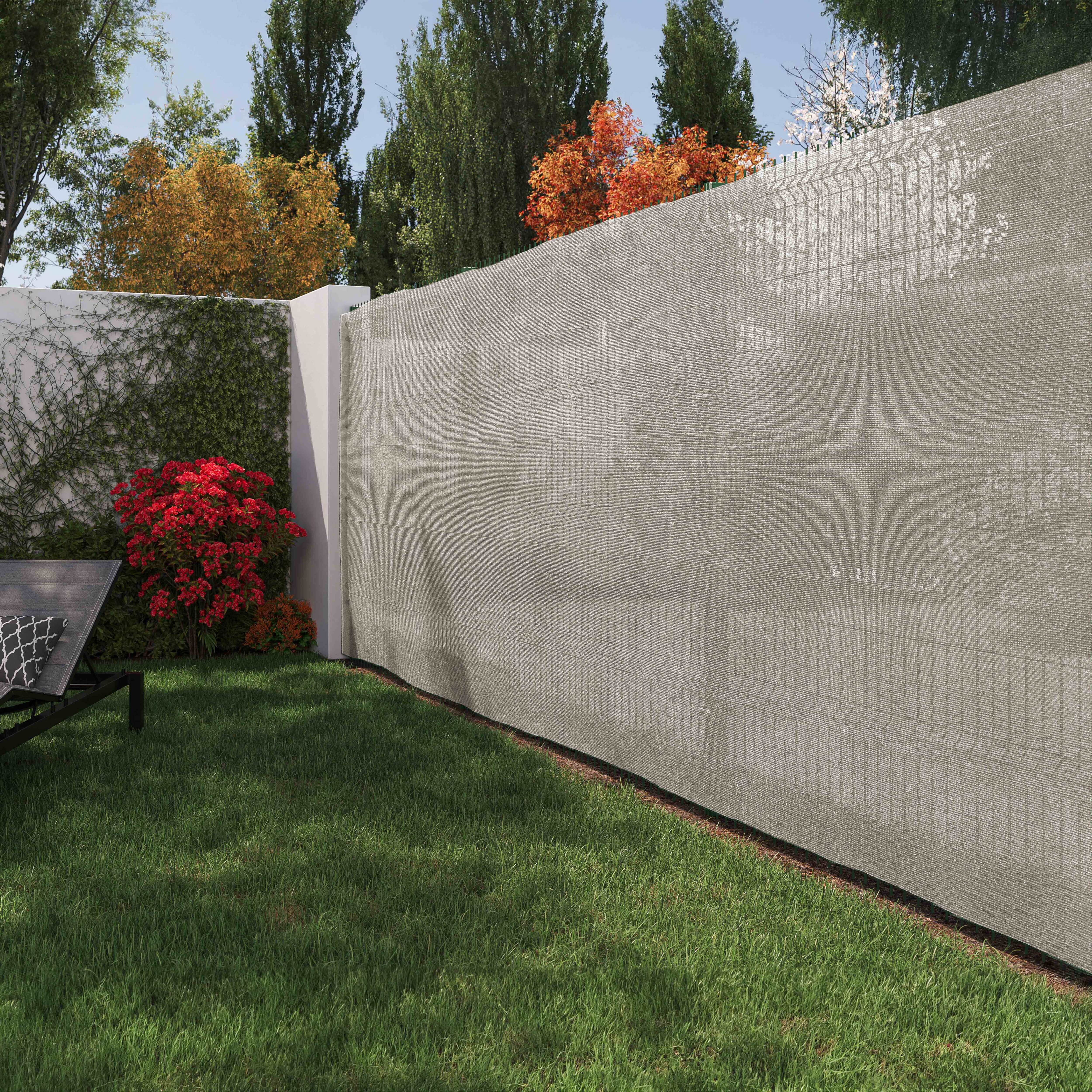 Eine Steinmauer und ein grauer Maschendrahtzaun in einem Garten, mit grünem Gras und Bäumen.