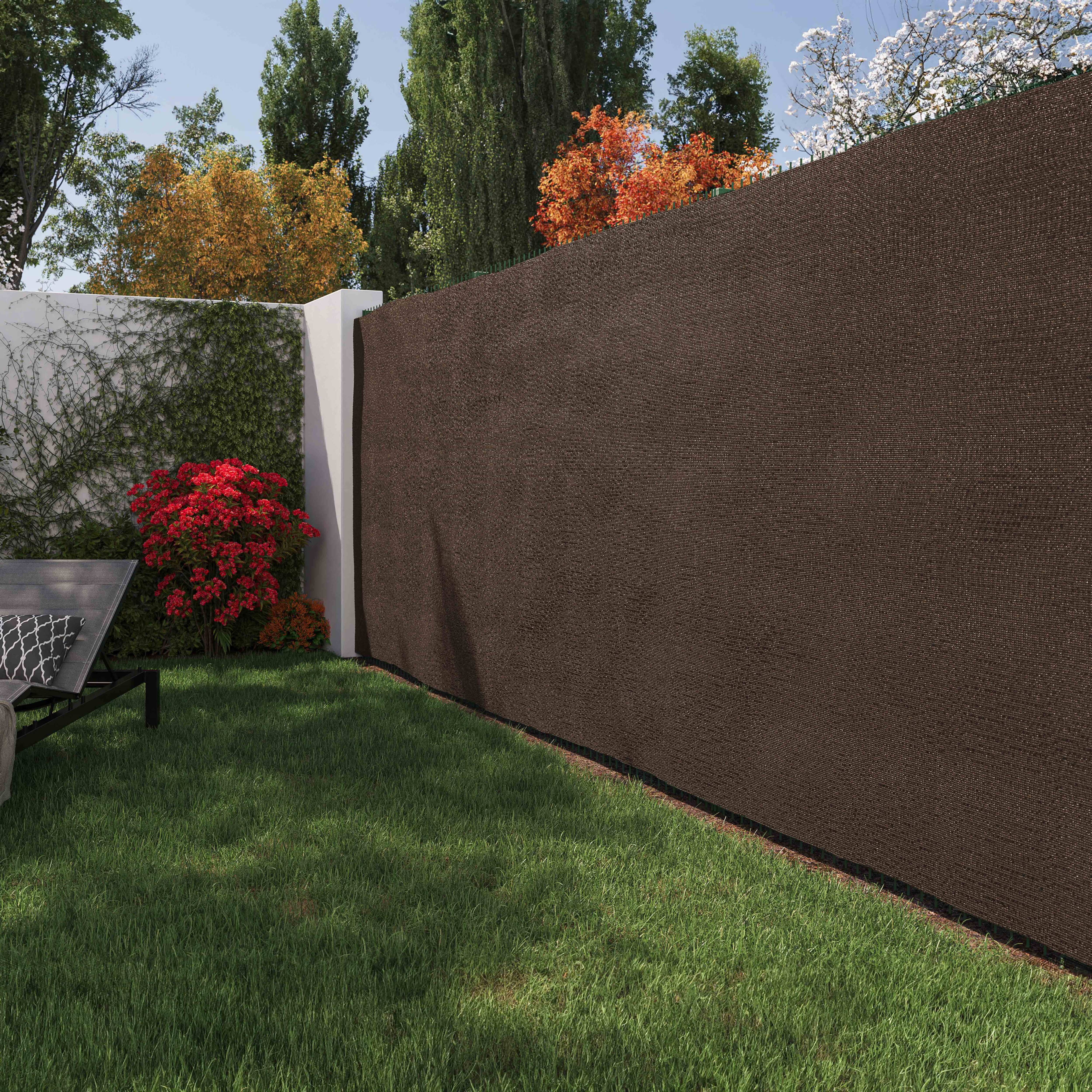Ein Garten mit braunem Zaun, grünem Gras und einer weißen Mauer. Bäume und Pflanzen sind im Hintergrund.