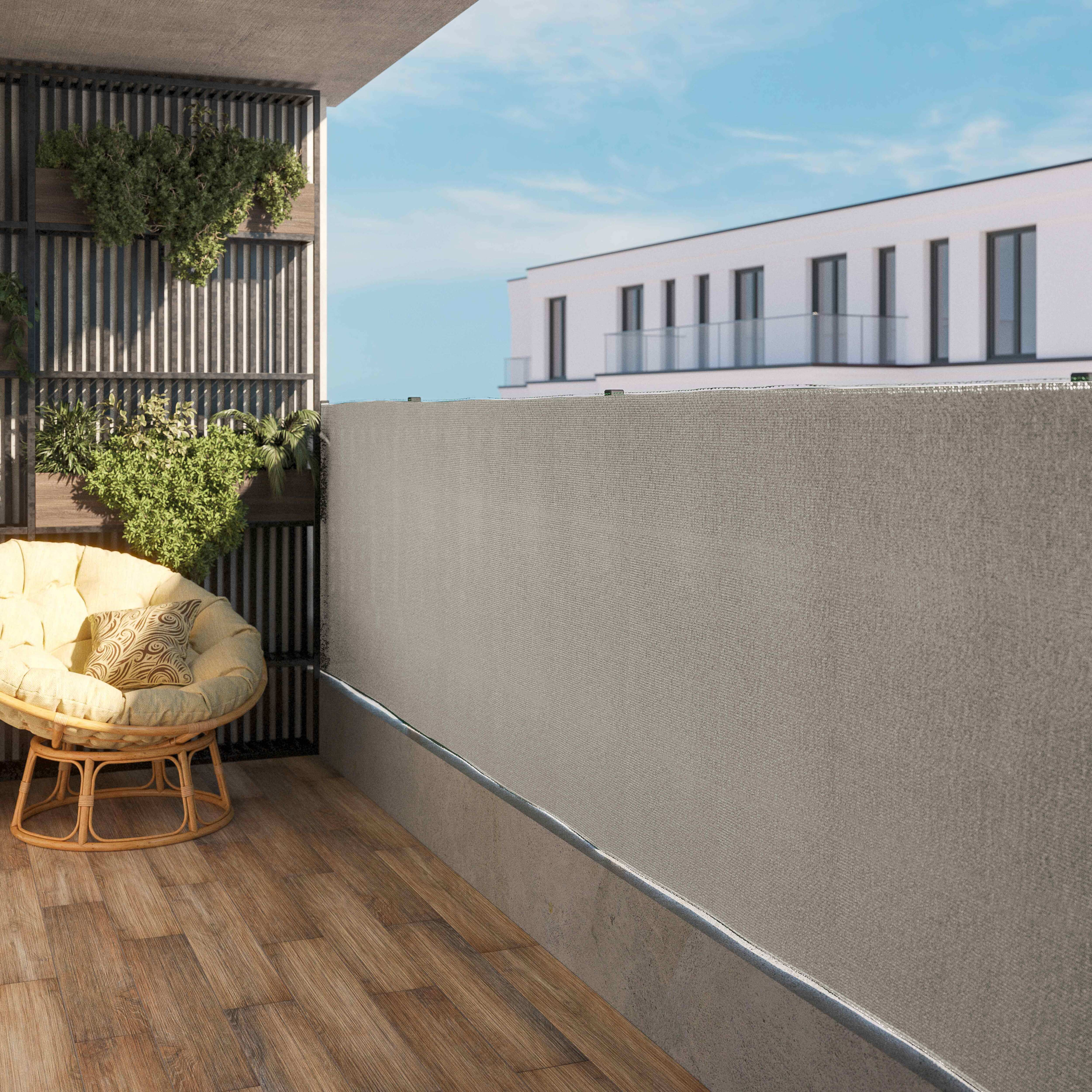 Grauer Sichtschutz auf einem Balkon. Holzboden, Stuhl und Pflanzen. Gebäude und blauer Himmel im Hintergrund.