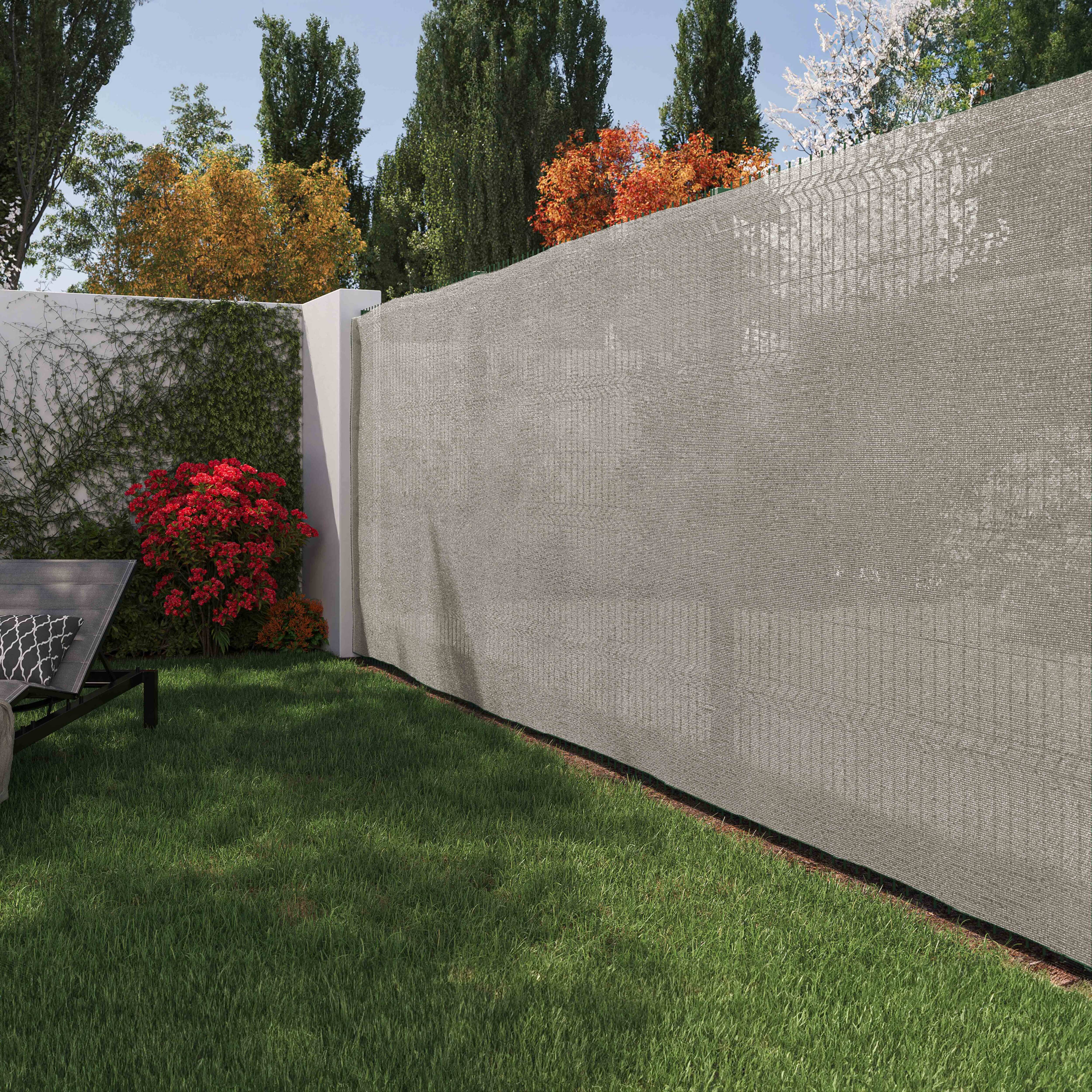 Ein grauer Sichtschutzzaun in einem Garten mit grünem Gras und einem roten Busch.