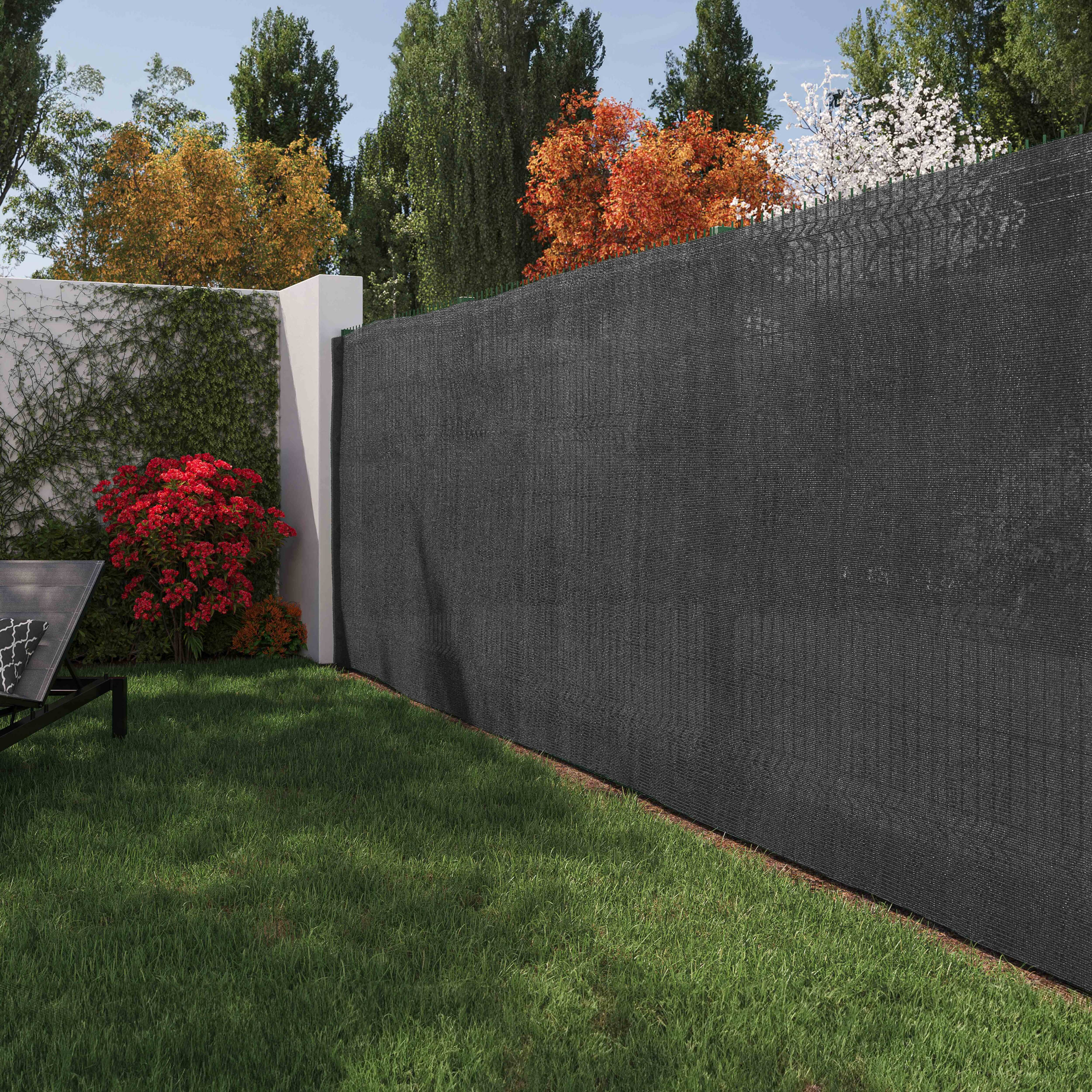 Ein Garten mit schwarzem Zaun und grünem Gras, Bäumen und einer Wand mit roten Büschen.