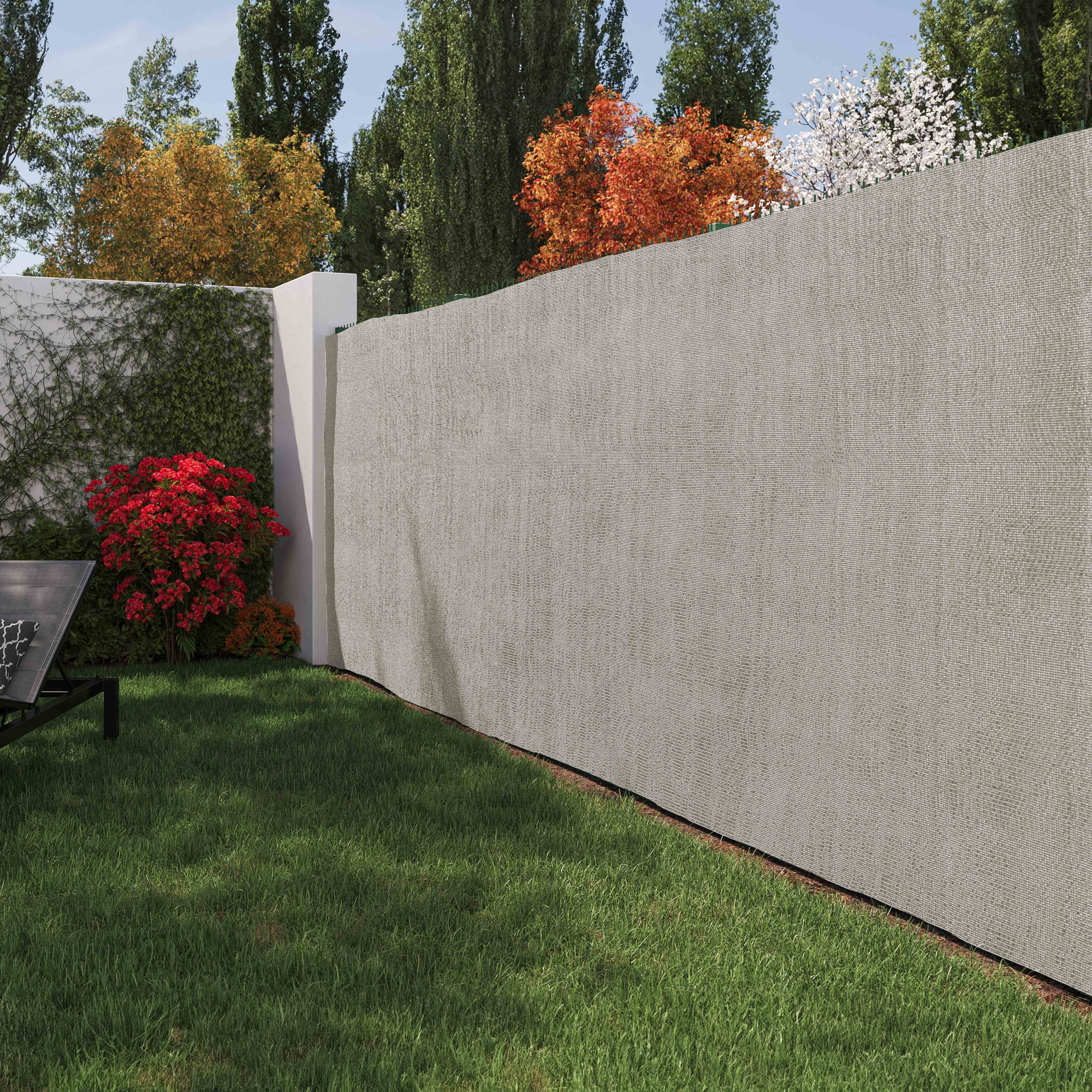 Ein Garten mit beigem Zaun und grünem Gras, Bäumen und einer Wand mit roten Büschen.