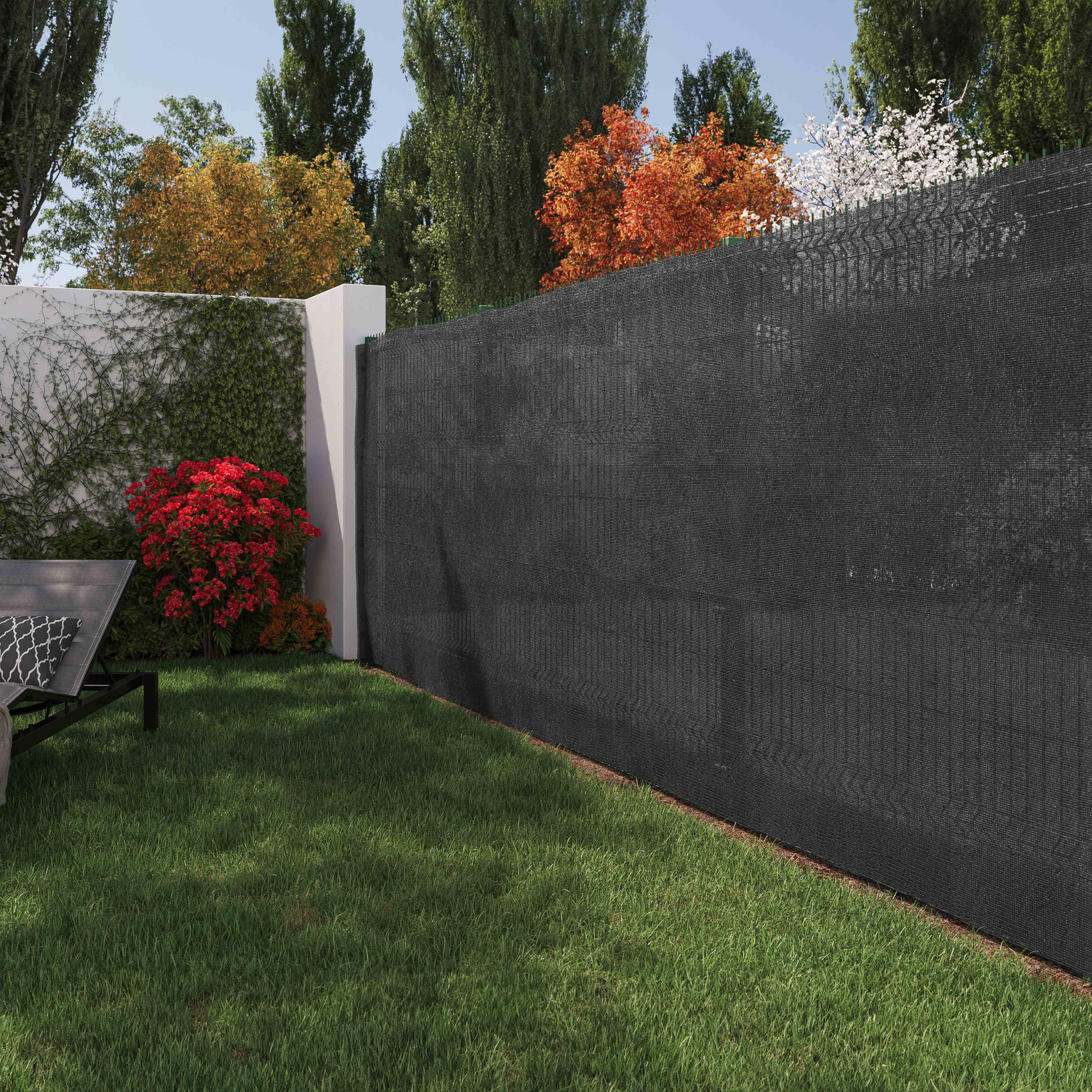 Ein Garten mit schwarzem Zaun und grünem Gras, Bäumen und einer Wand mit roten Büschen.