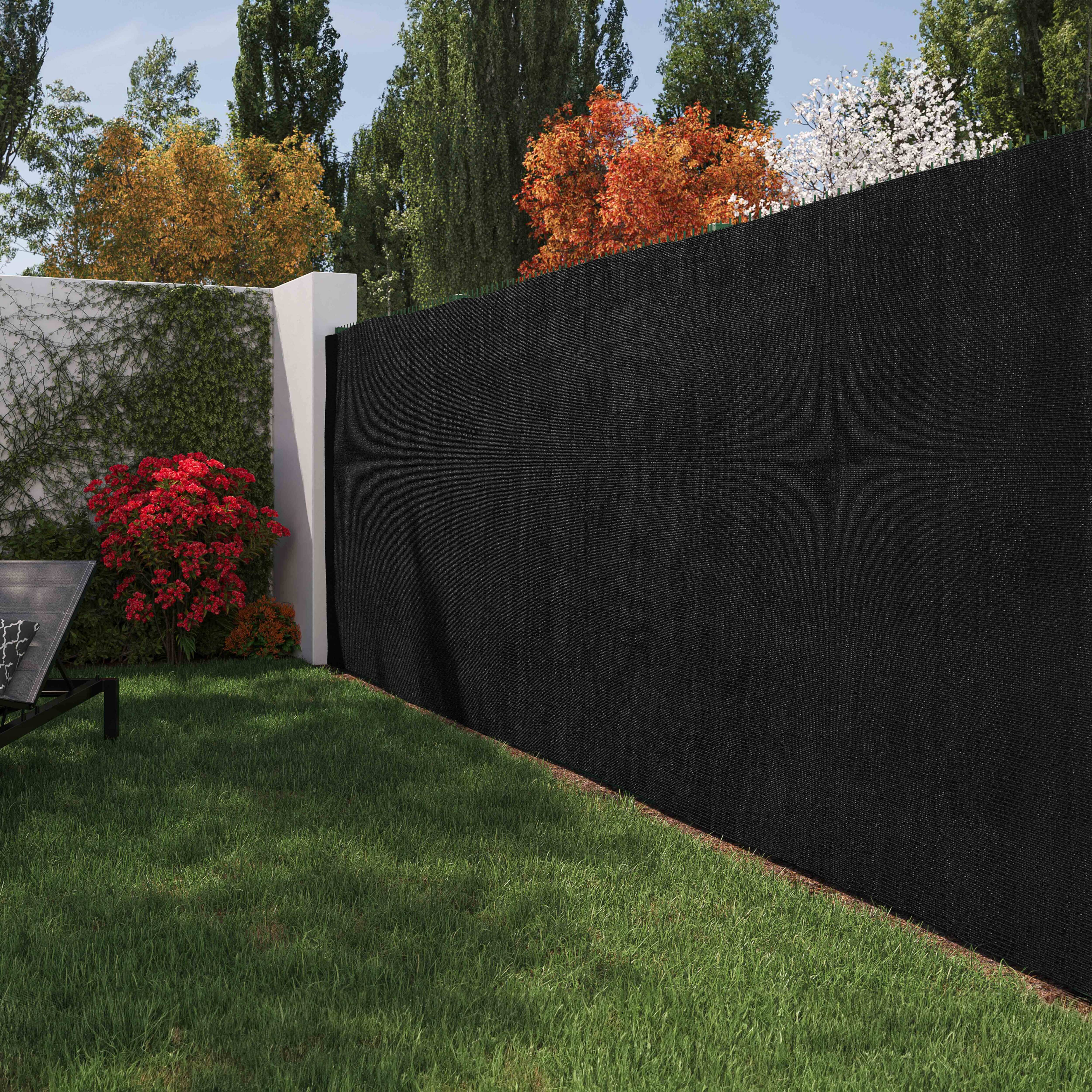 Ein Garten mit schwarzem Zaun und grünem Gras, Bäumen und einer Wand mit roten Büschen.
