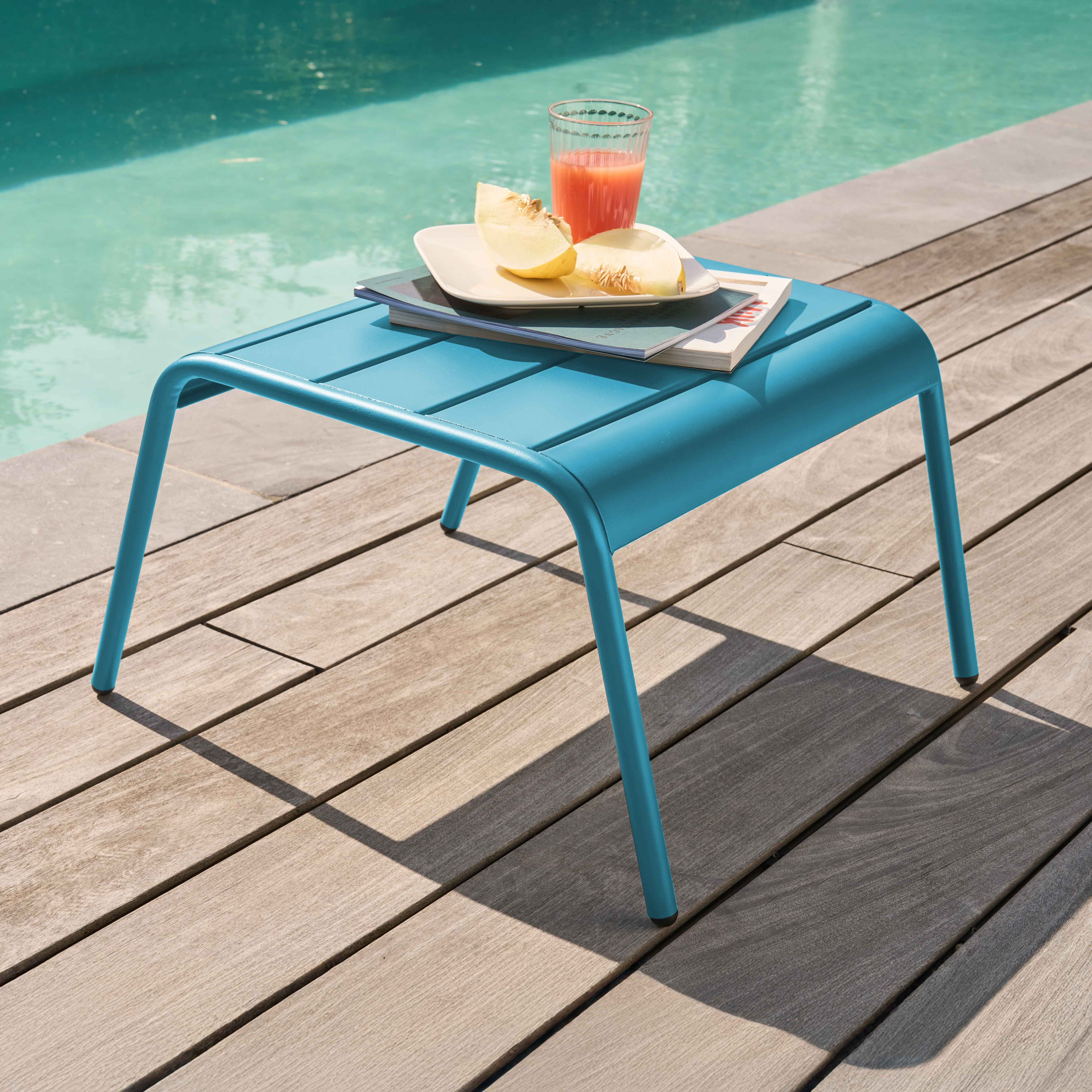 Blauer Tisch mit Lattenrost neben Pool. Glas Saft, Obst liegen darauf.