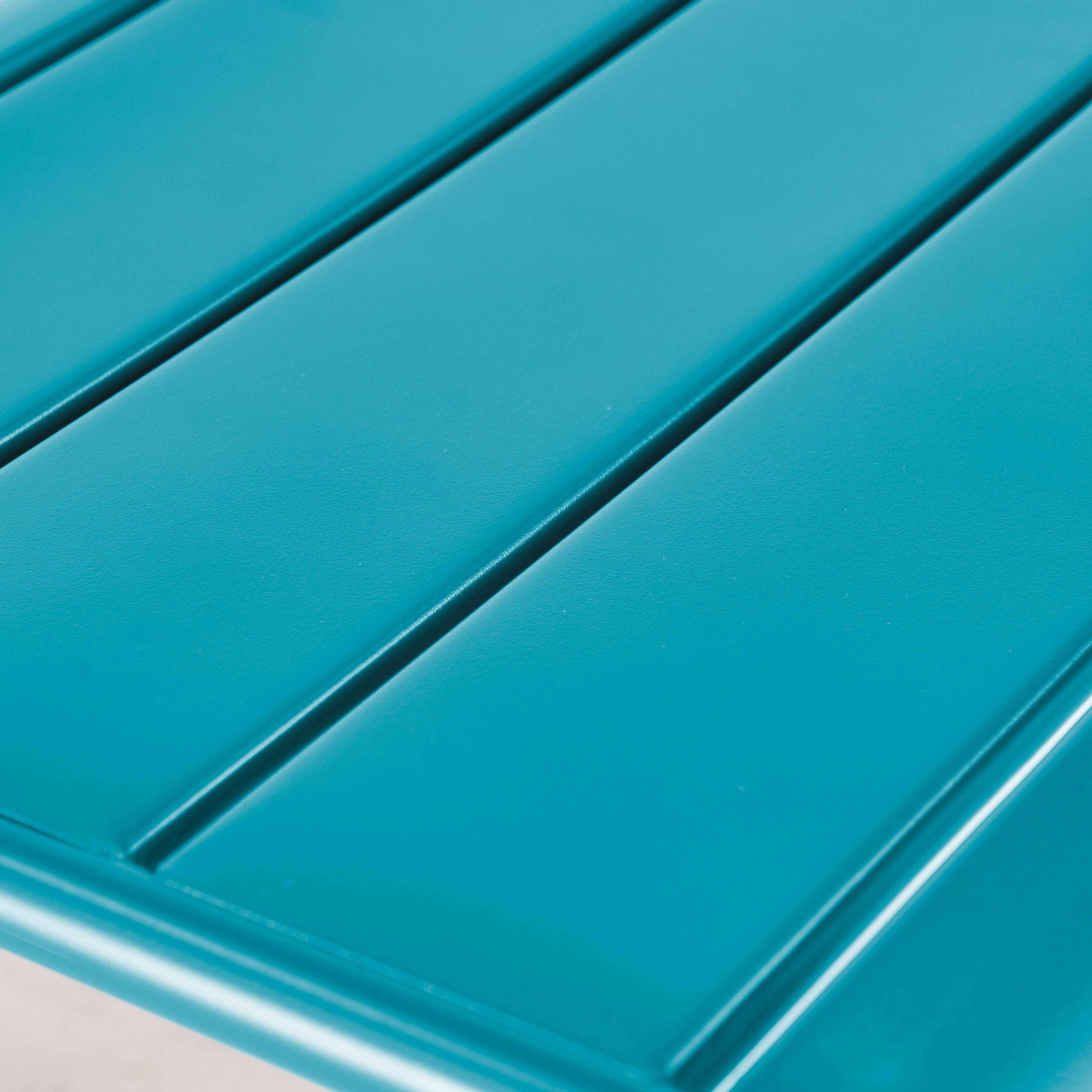 Nahaufnahme einer türkisfarbenen Metalltischplatte mit drei horizontalen Lamellen.