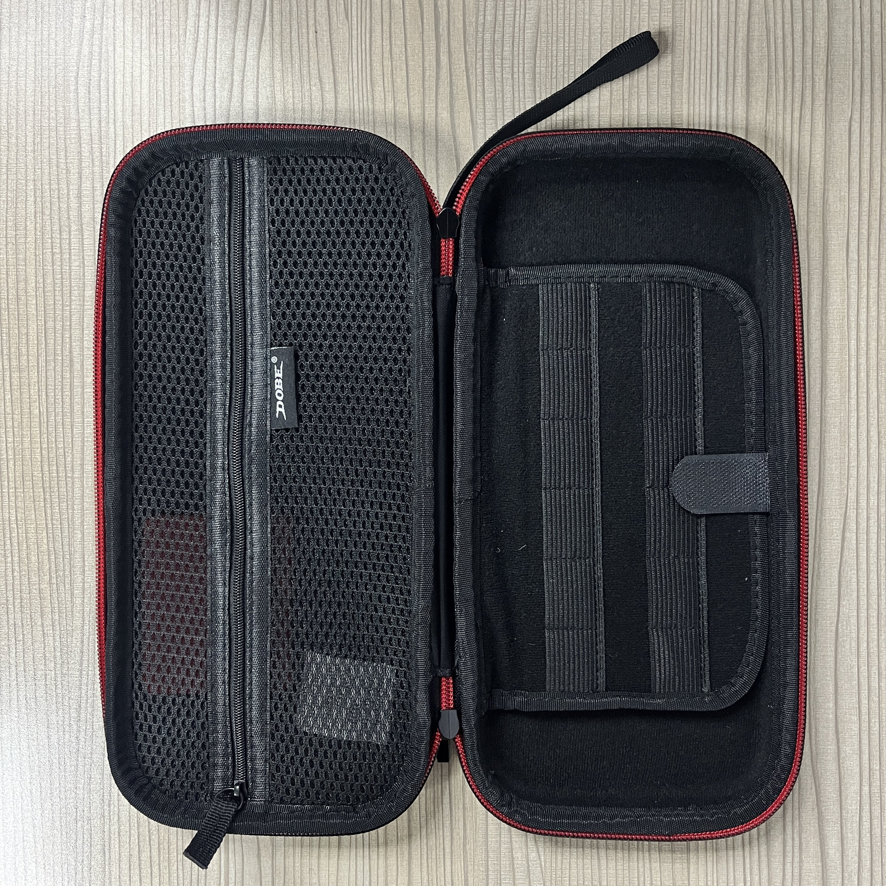 Otwarta obudowa z siatkową kieszenią i mniejszą obudową w środku. Czerwone wykończenie. Drewniane tło.