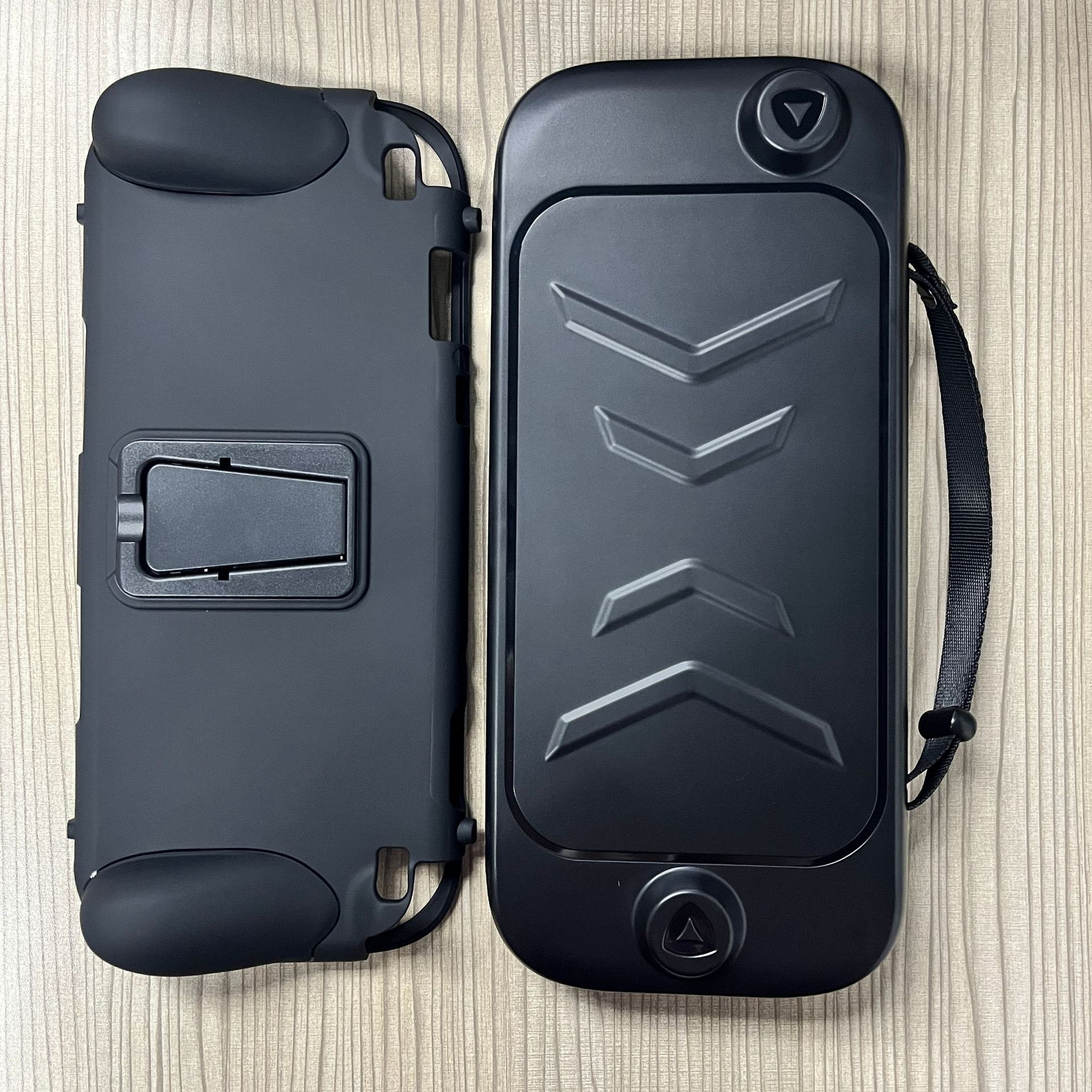 Zwei schwarze Handheld-Konsolenhüllen. Eine hat einen Riemen und Chevron-Design. Die andere hat einen Ständer.
