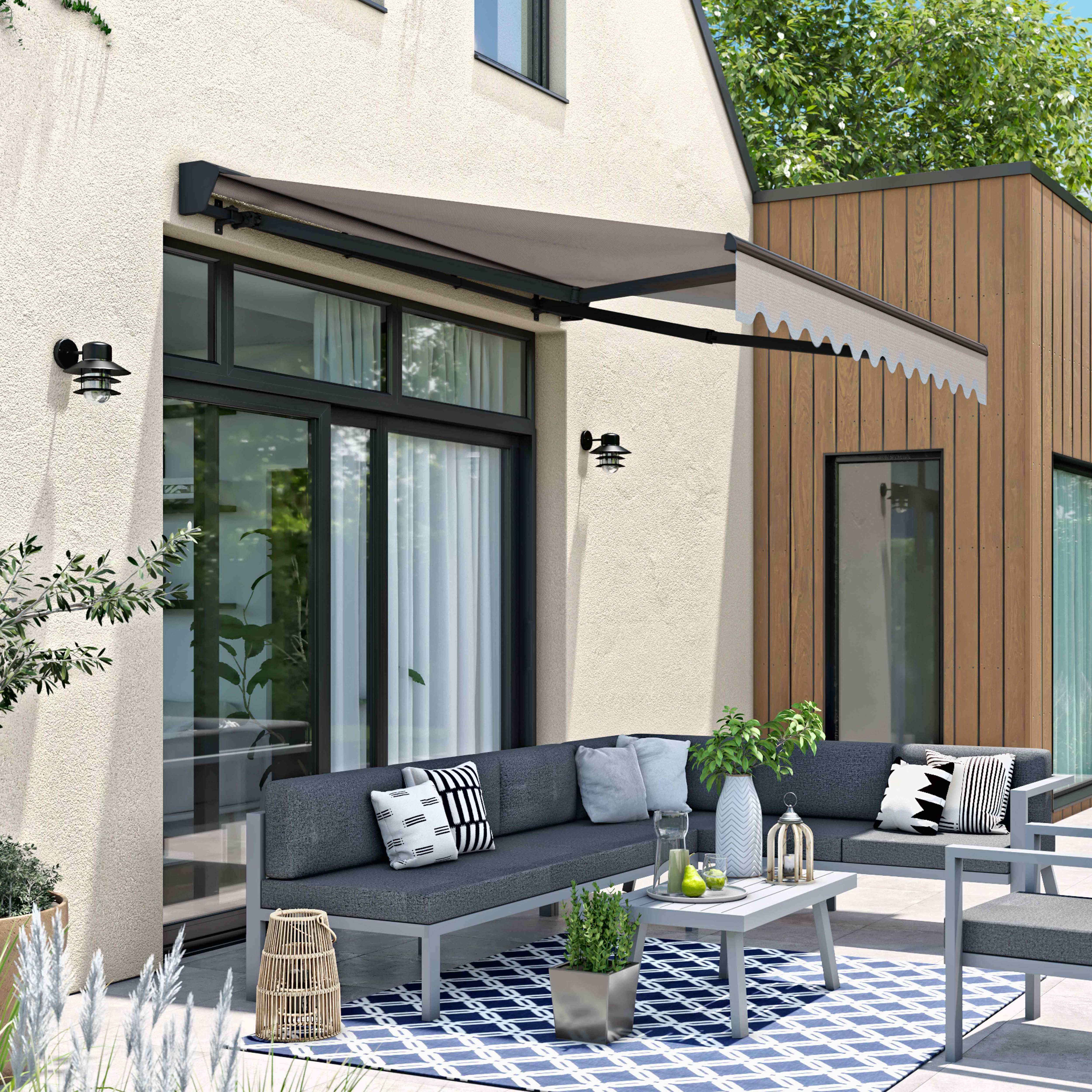 Eine Terrasse mit Möbeln, Markise und Grün. Ein graues Sofa, ein weißer Tisch und ein blau-weißer Teppich sind sichtbar.