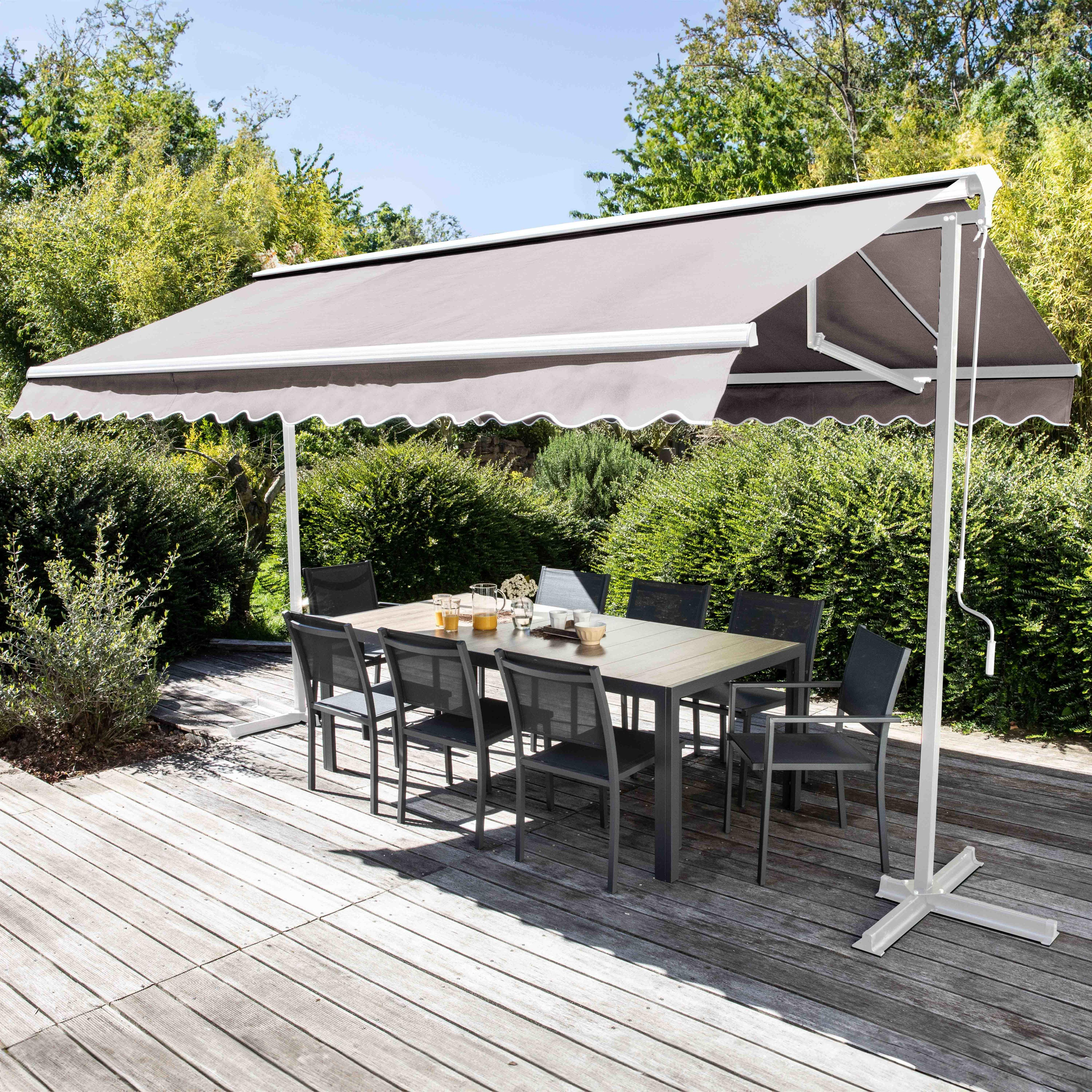 Eine Terrasse mit großem Vordach, Tisch, Stühlen und Pflanzen. Das Vordach ist grau, Tisch und Stühle sind dunkel.