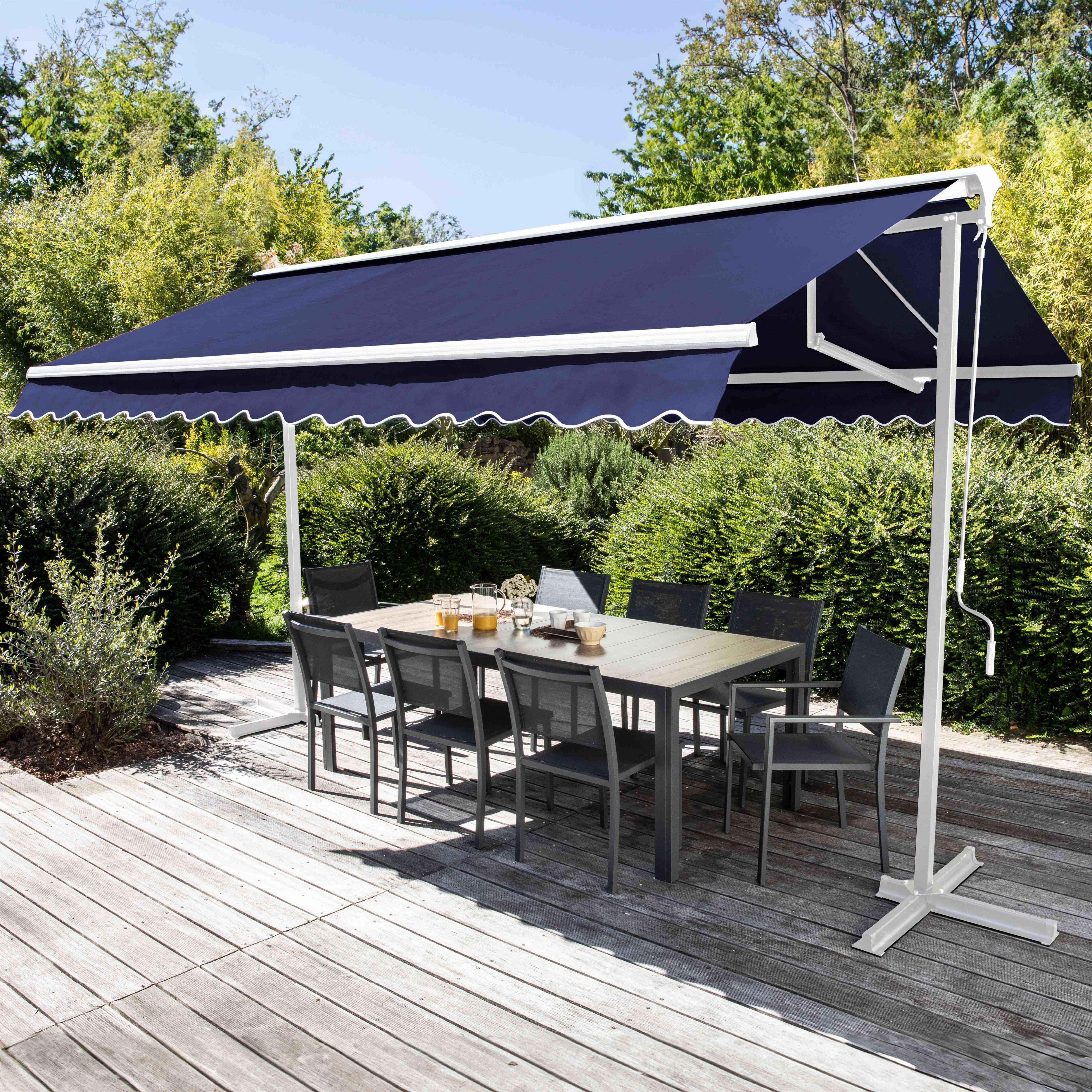 Gartenmöbel unter einer blauen Markise auf einer Holzterrasse, umgeben von Grün und Bäumen.