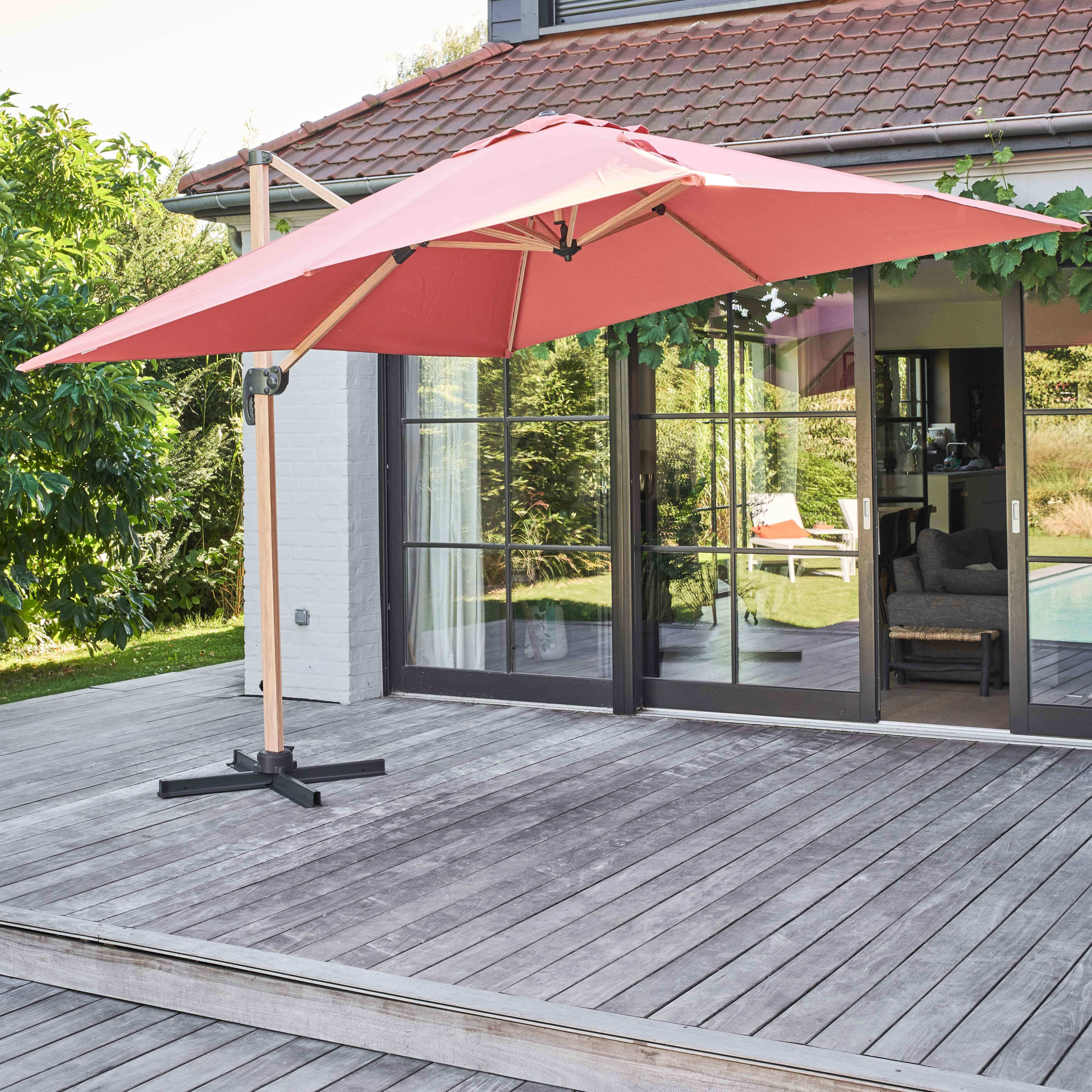 Rosa Ausleger-Sonnenschirm auf Holzdeck in der Nähe eines Hauses mit Glastüren.