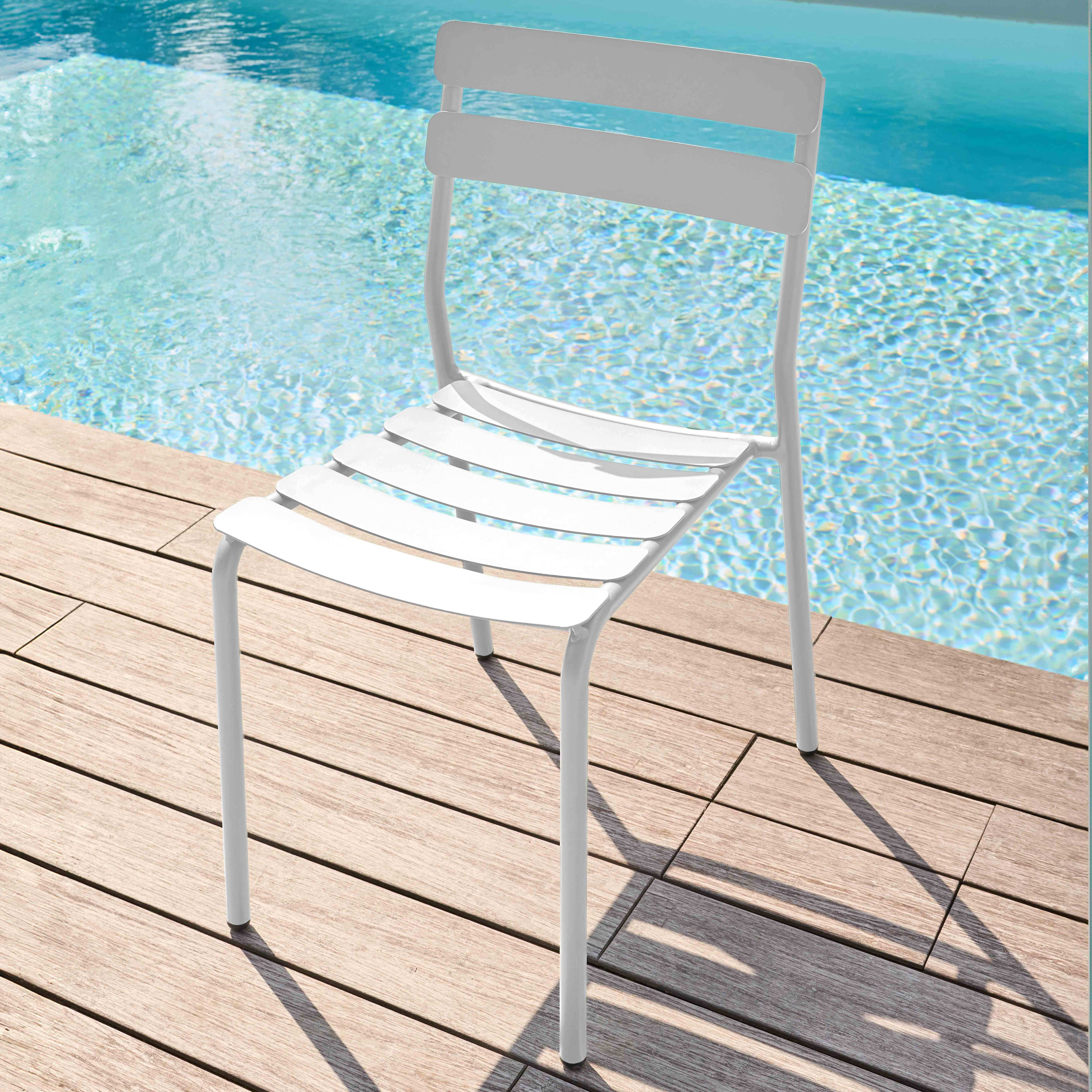 Weißer Outdoor-Stuhl auf Holzdeck, blauer Pool im Hintergrund.