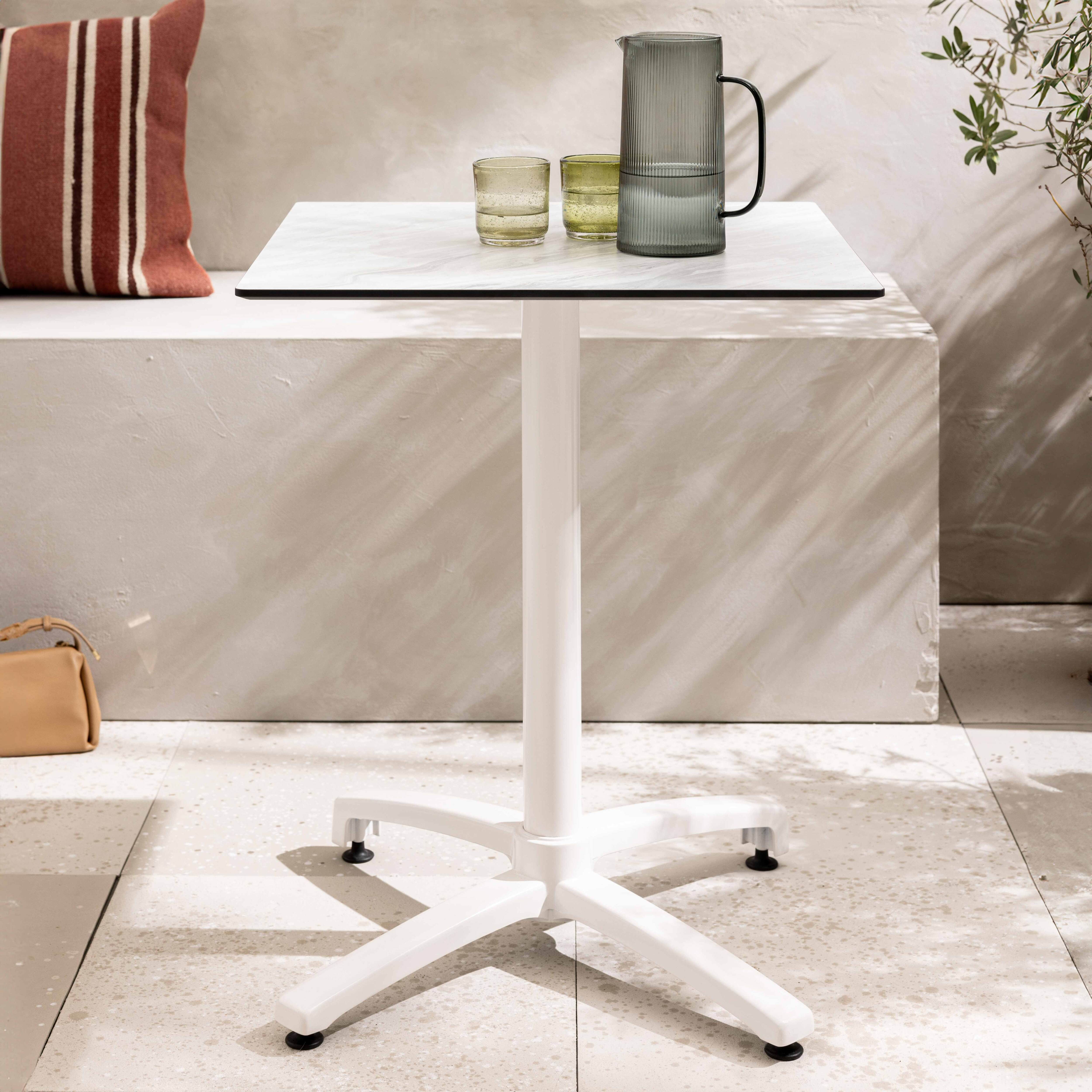 Weißer quadratischer Tisch mit Glaskaraffe und Gläsern.