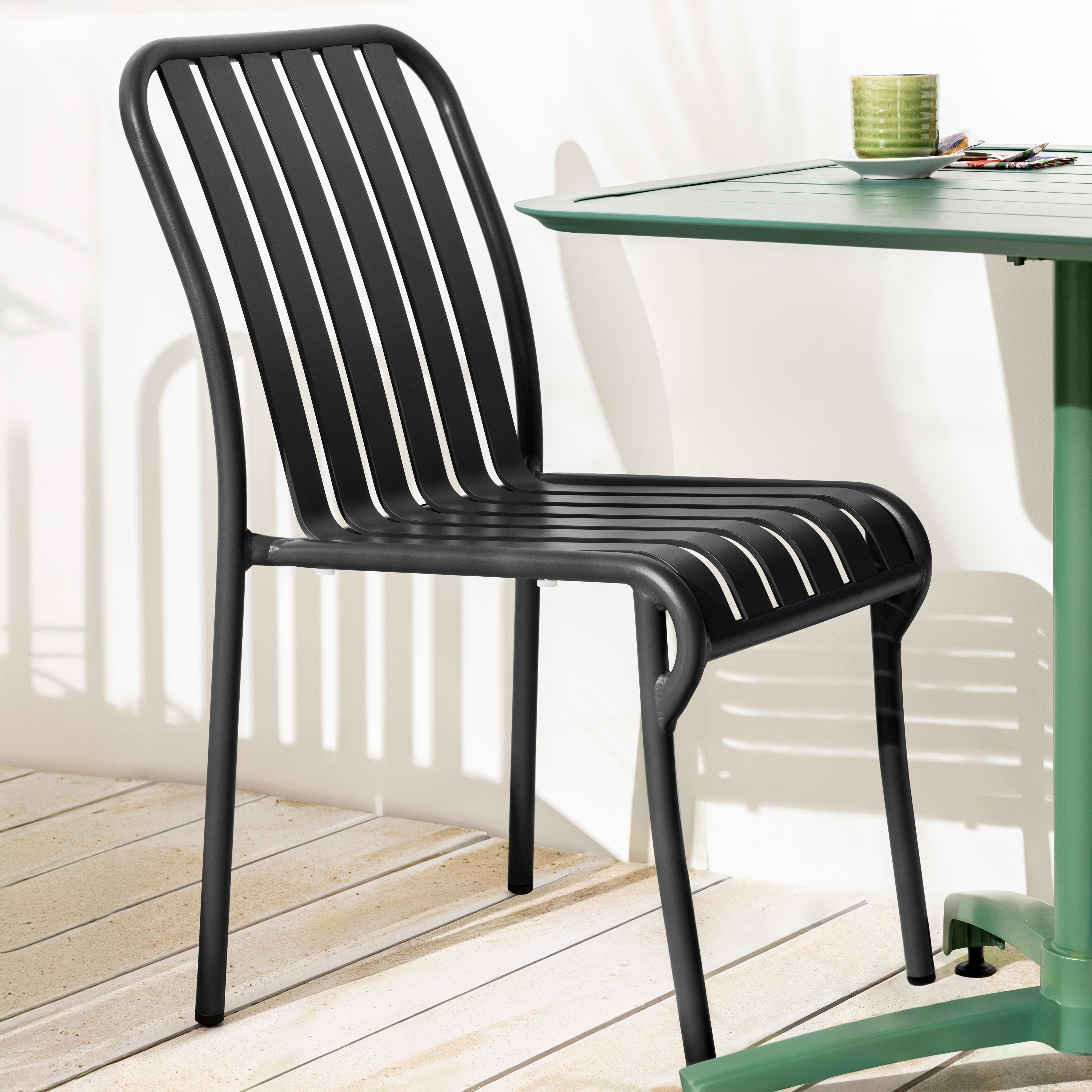 Schwarzer Metallstuhl mit vertikalen Lamellen und ein grüner Tisch auf Terrasse.