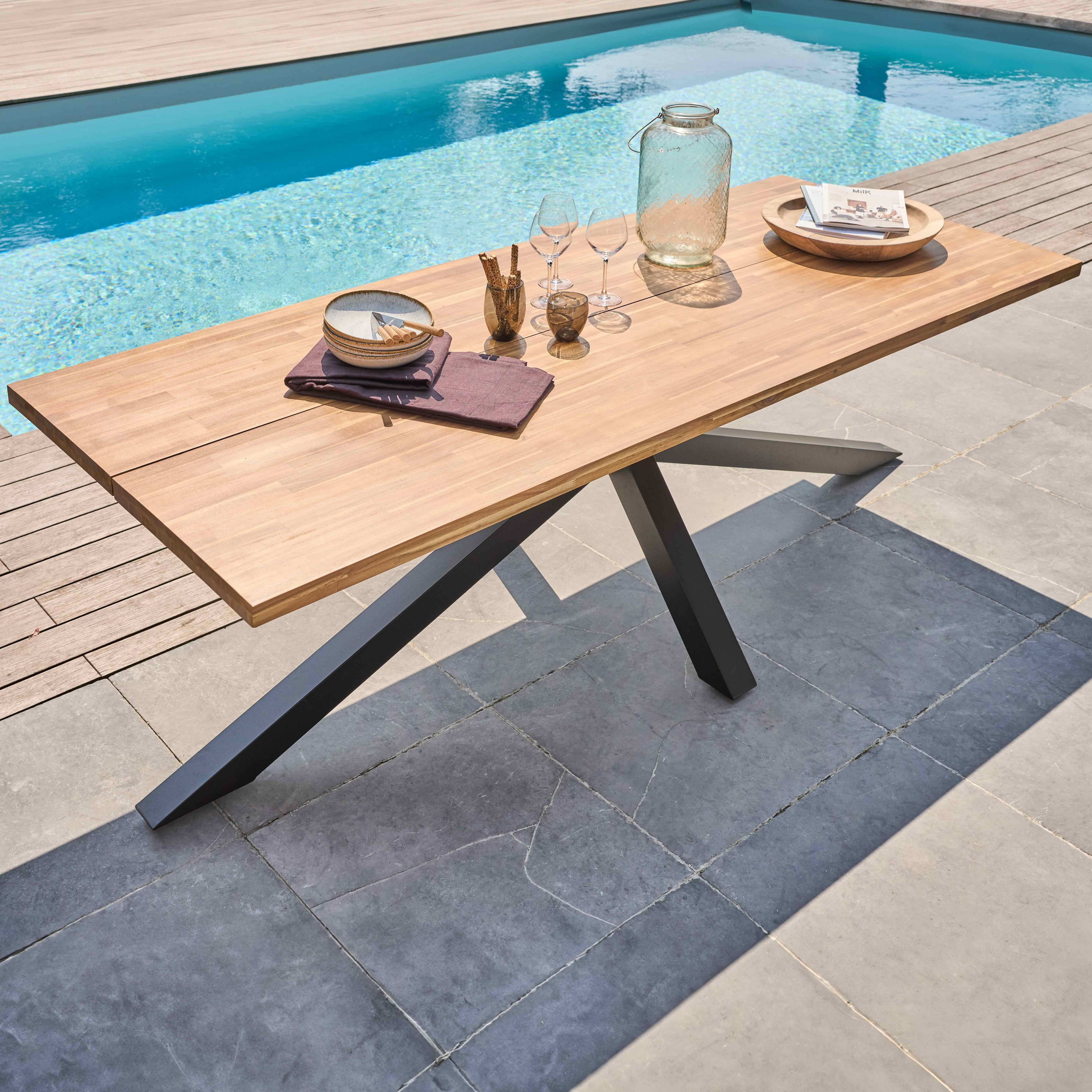 Holz-Esstisch für draußen mit schwarzen Beinen, in der Nähe eines Pools, mit Gegenständen.