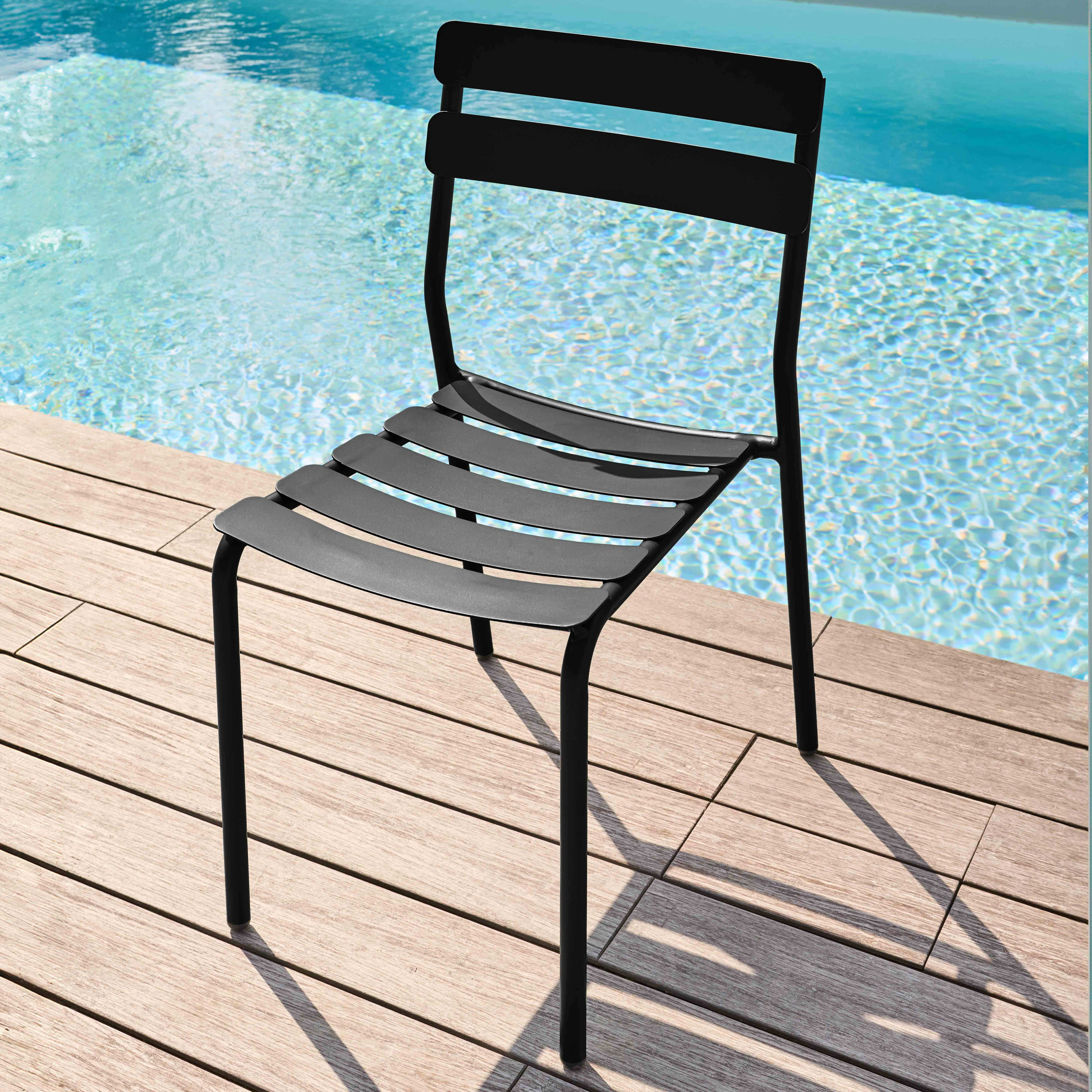 Schwarzer Stuhl am Pool. Lamellen-Sitz, schwarzer Rahmen und drei Rückenlatten. Holzdeck und Wasser im Blick.