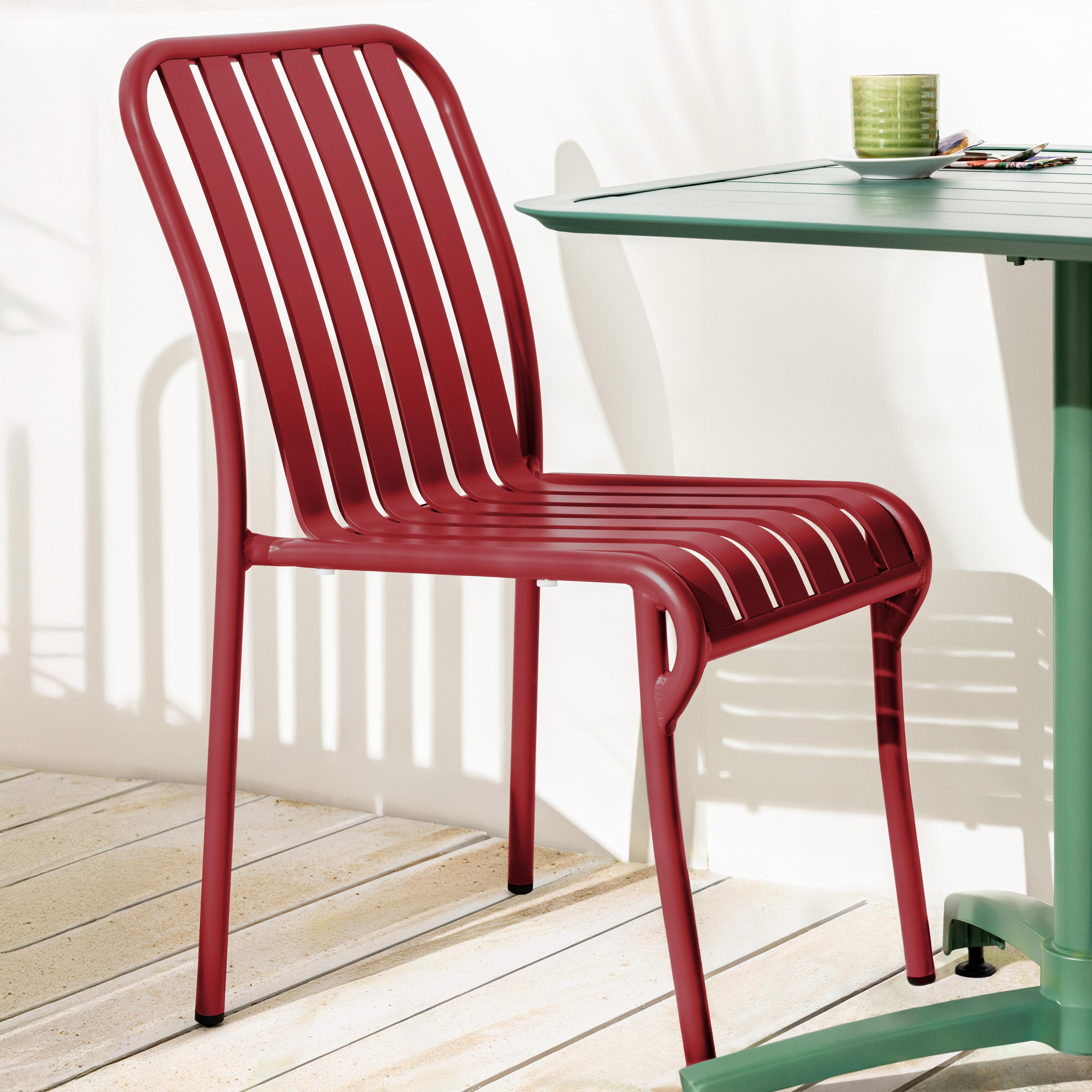 Roter Metallstuhl neben einem grünen Tisch. Auf dem Tisch stehen ein Glas und eine Tasse. Holzfußboden.