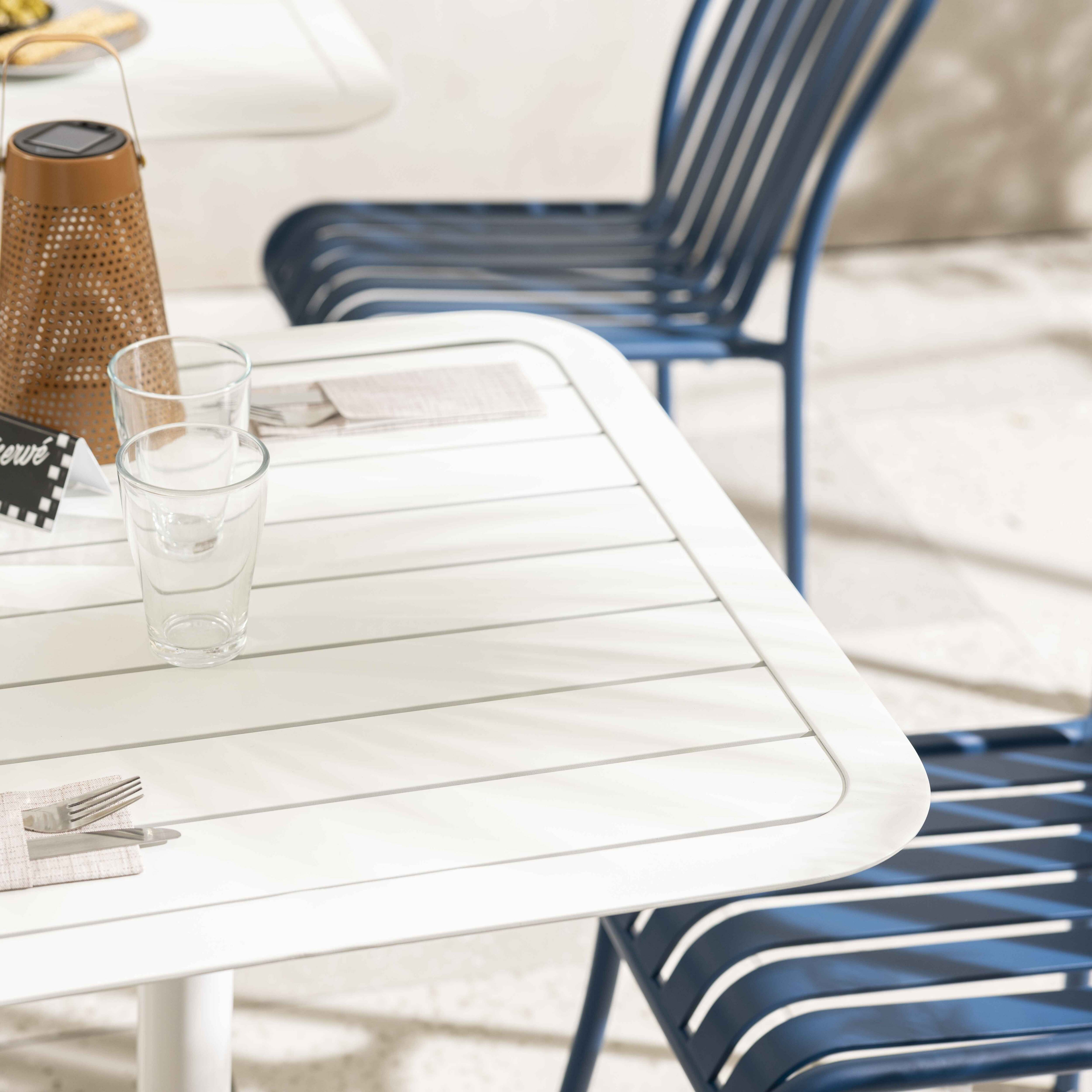 Weißer Tisch mit Gläsern, Besteck und blauem Stuhl im Hintergrund.