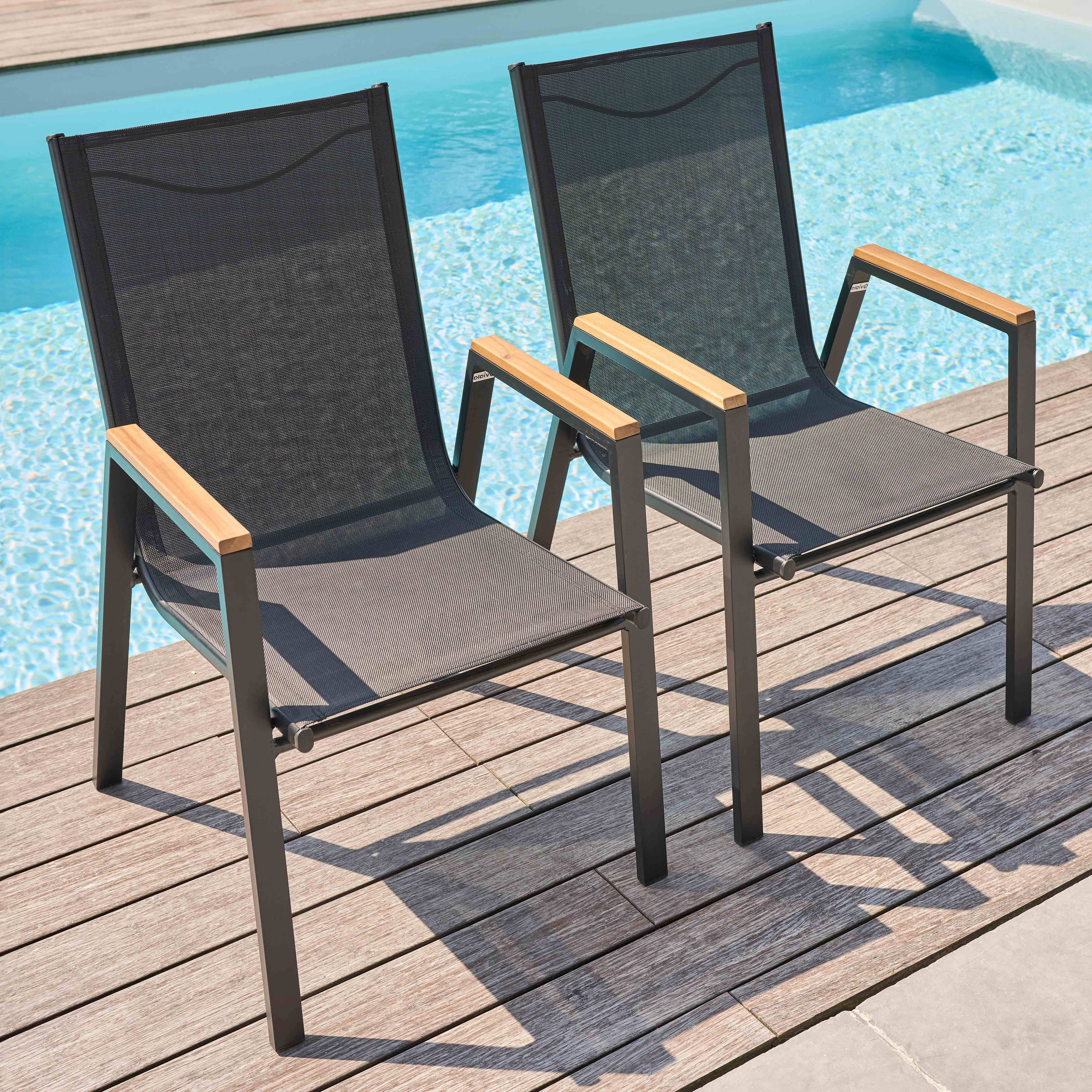 Zwei schwarze Netzstühle mit Holzarmlehnen stehen am Pool.