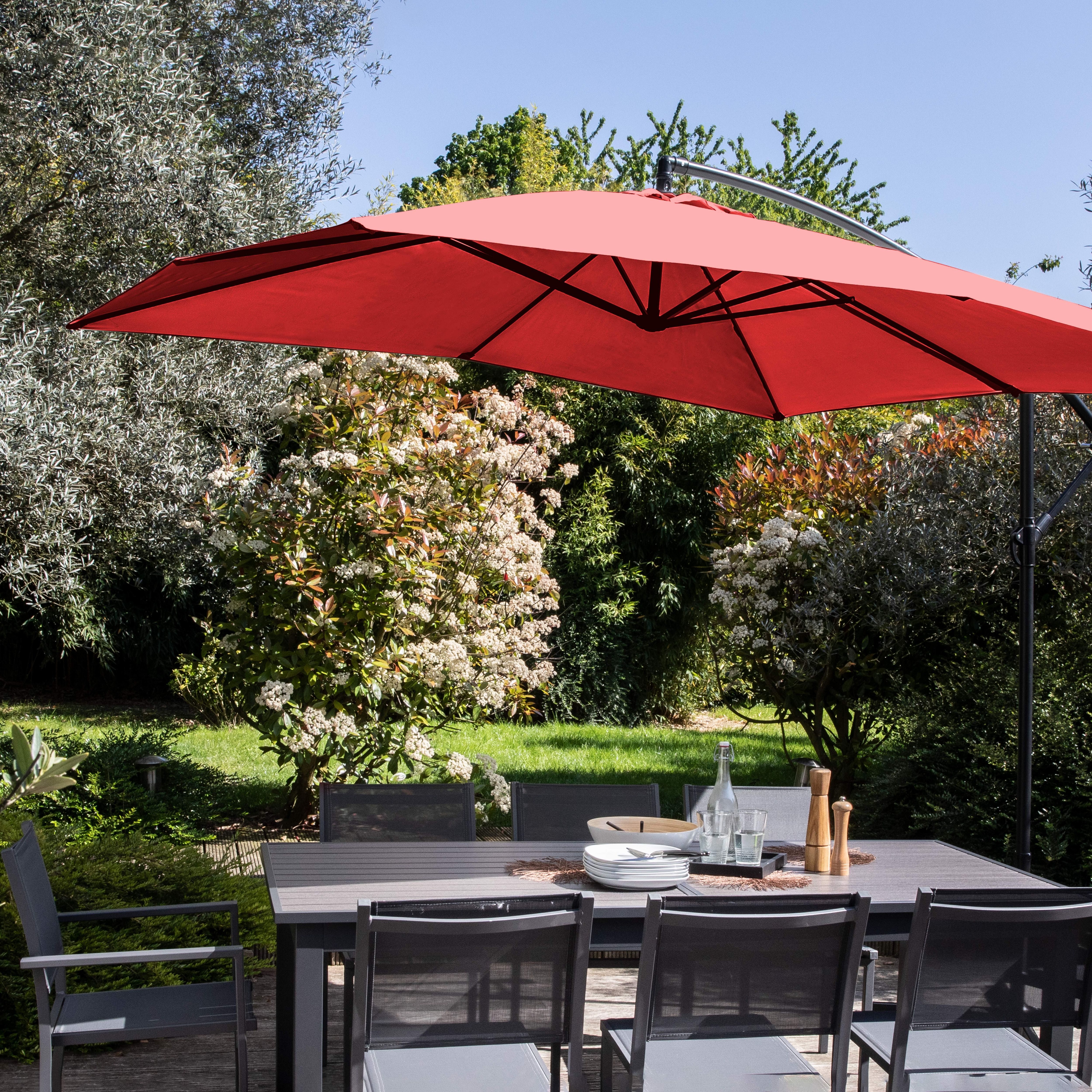 Roter Regenschirm über Tisch, Garteneinstellung mit Bäumen und Stühlen.