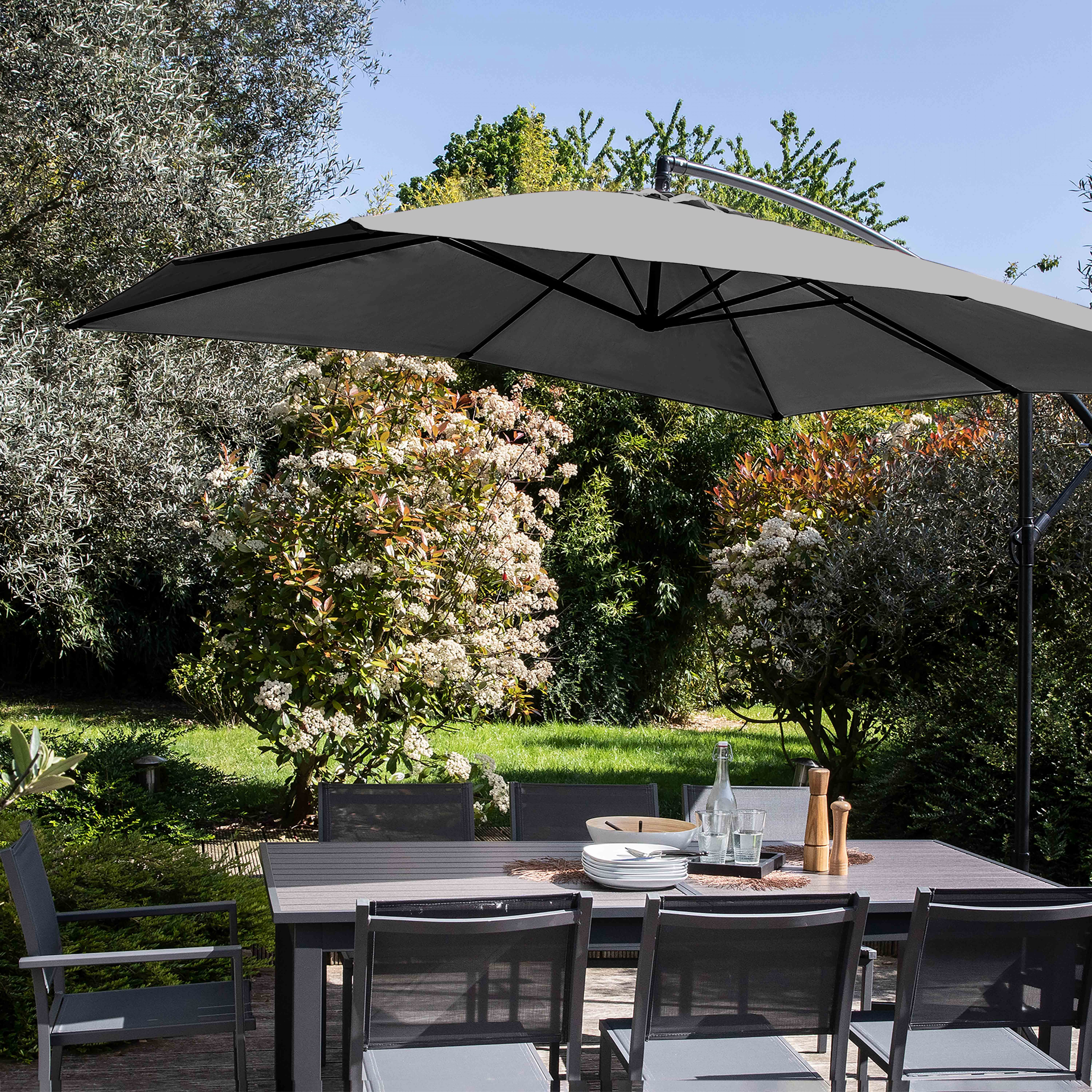 Essplatz im Freien mit Tisch, Stühlen und großem grauen Sonnenschirm. Bäume und Himmel im Hintergrund.