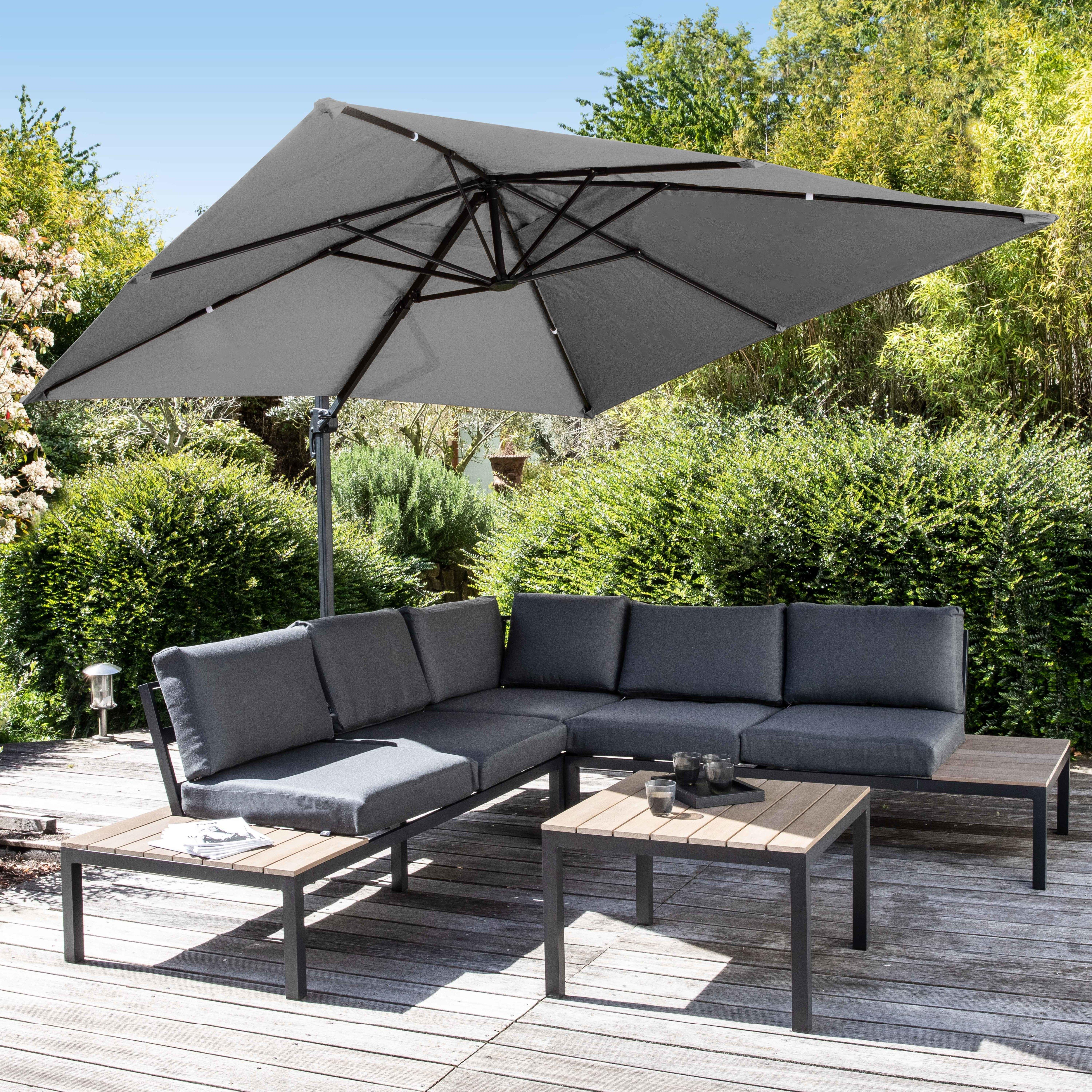 Ein graues Terrassenset mit einem großen Sonnenschirm und zwei Couchtischen steht auf einem Holzdeck.
