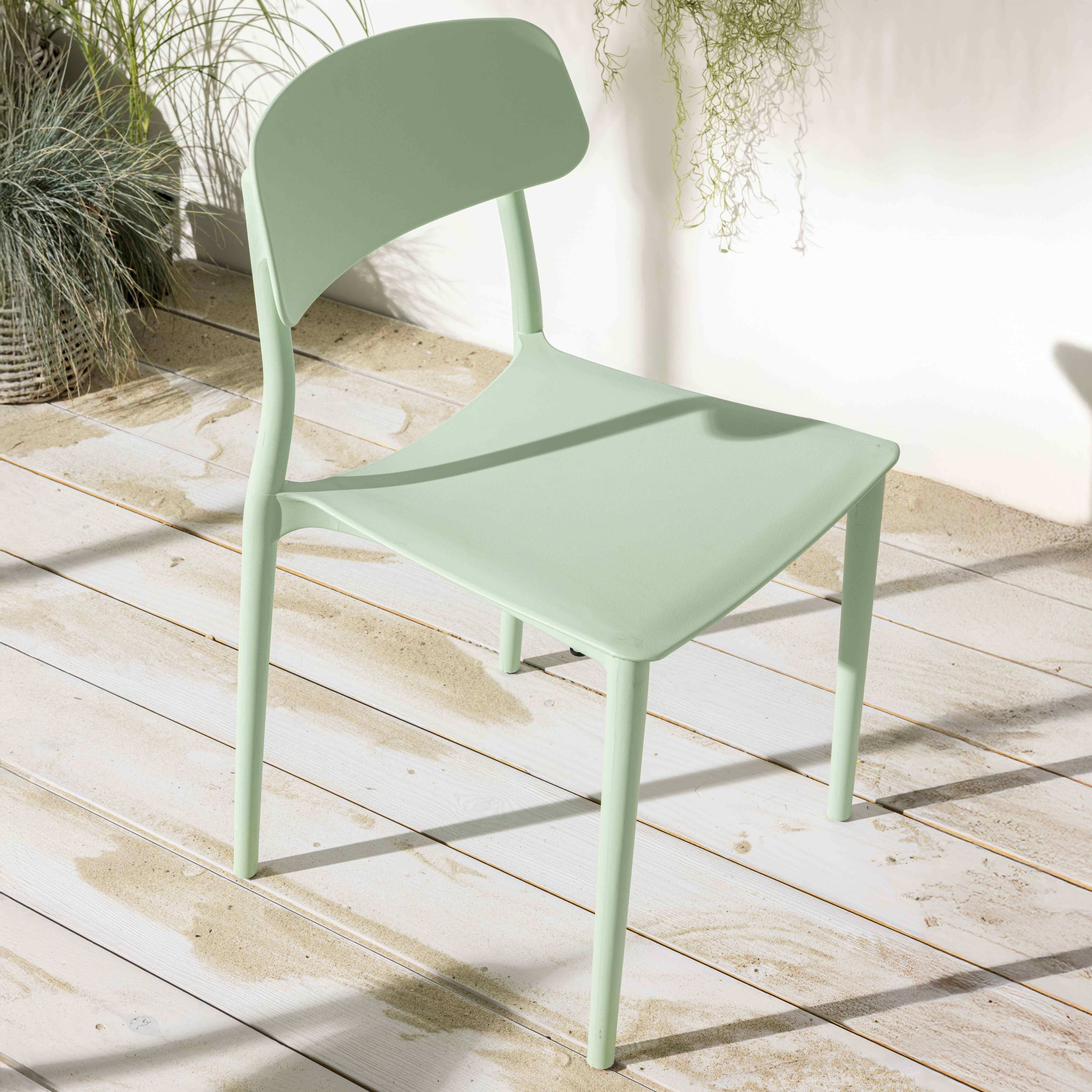 Mintgrüner Terrassenstuhl aus Kunststoff auf Holzdielen mit Pflanzen im Hintergrund.