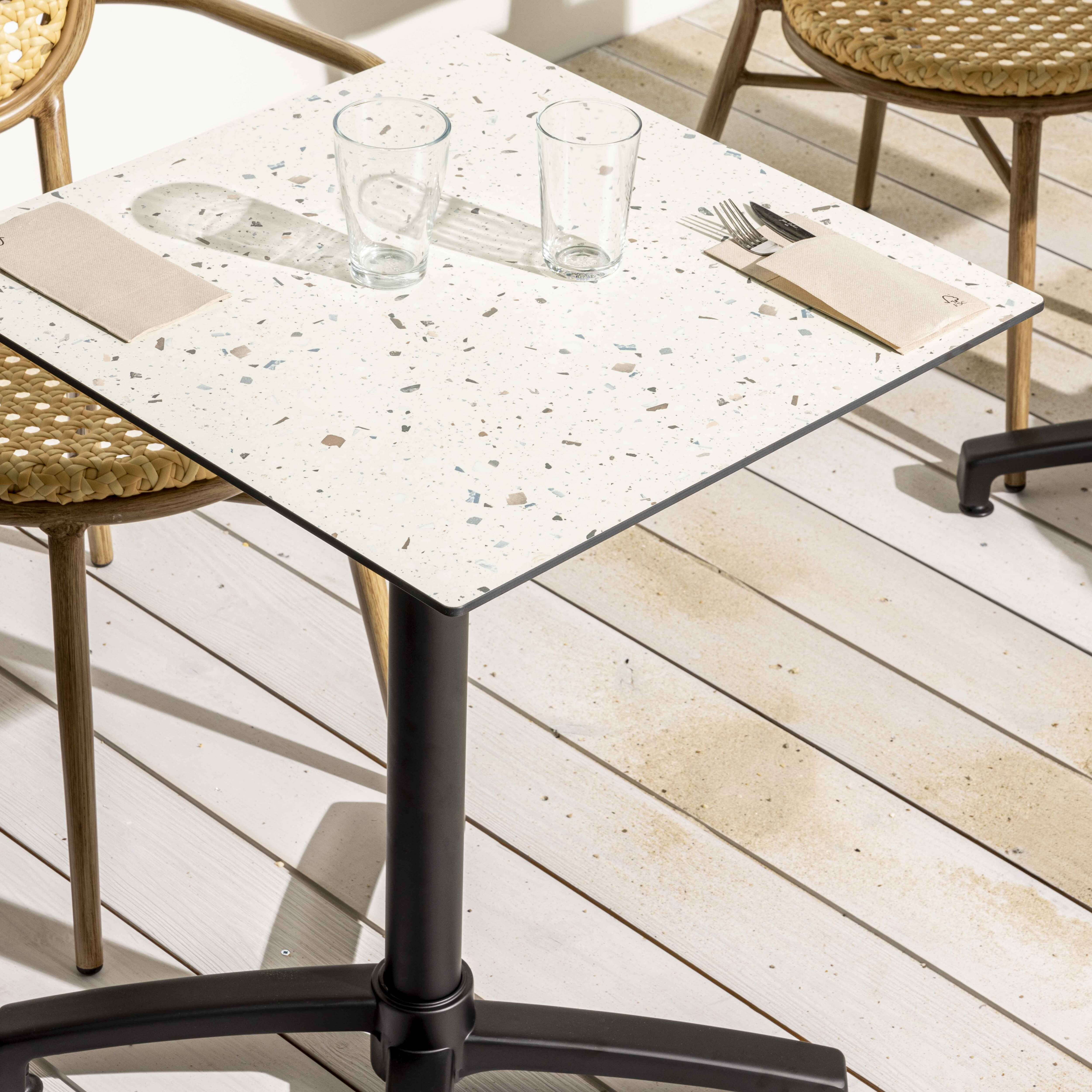 Quadratischer Tisch mit gesprenkelter weißer Oberfläche, Gläsern und Besteck auf Holzdeck.