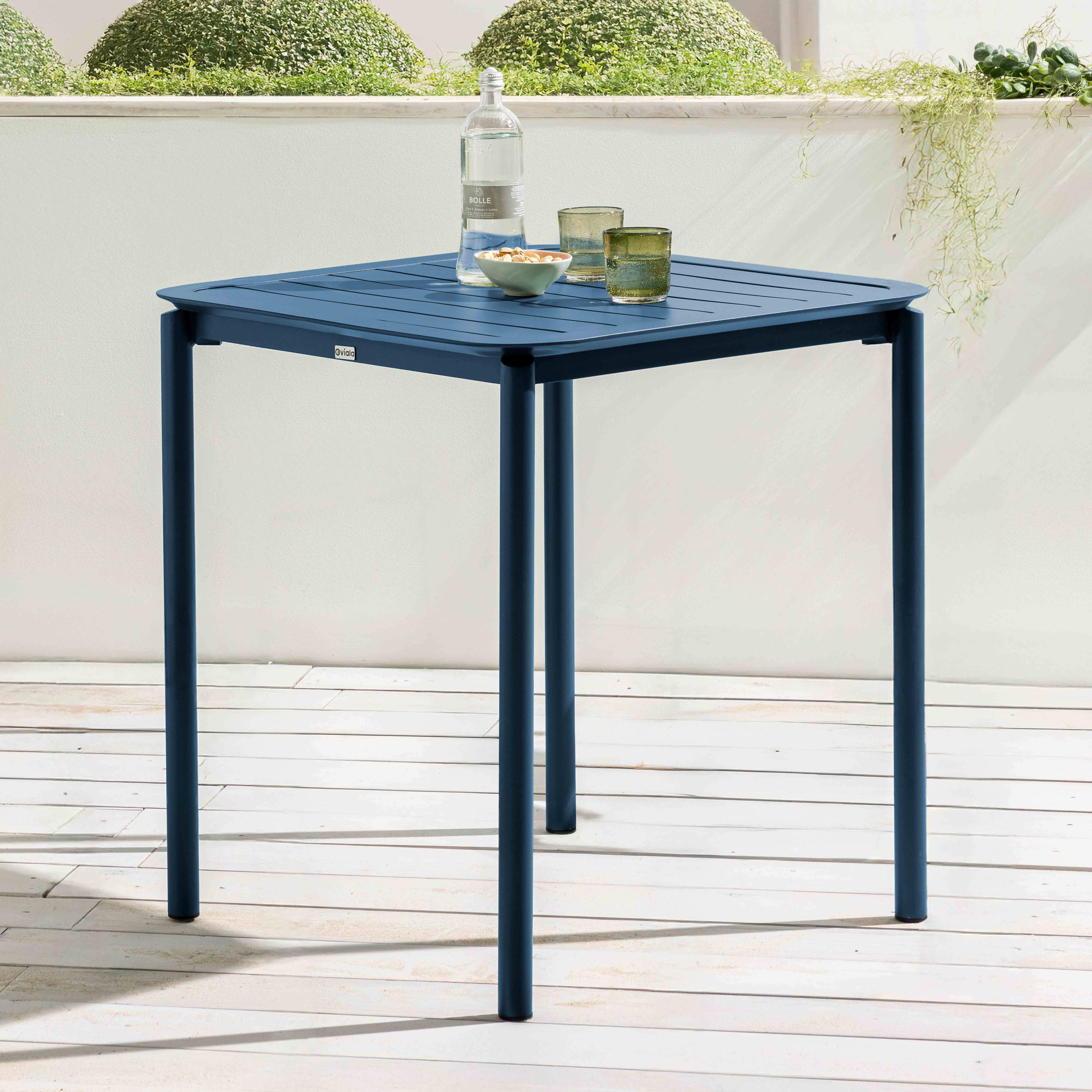 Blauer quadratischer Tisch mit vier Beinen. Es hat einen Gartenhintergrund mit Gegenständen darauf.