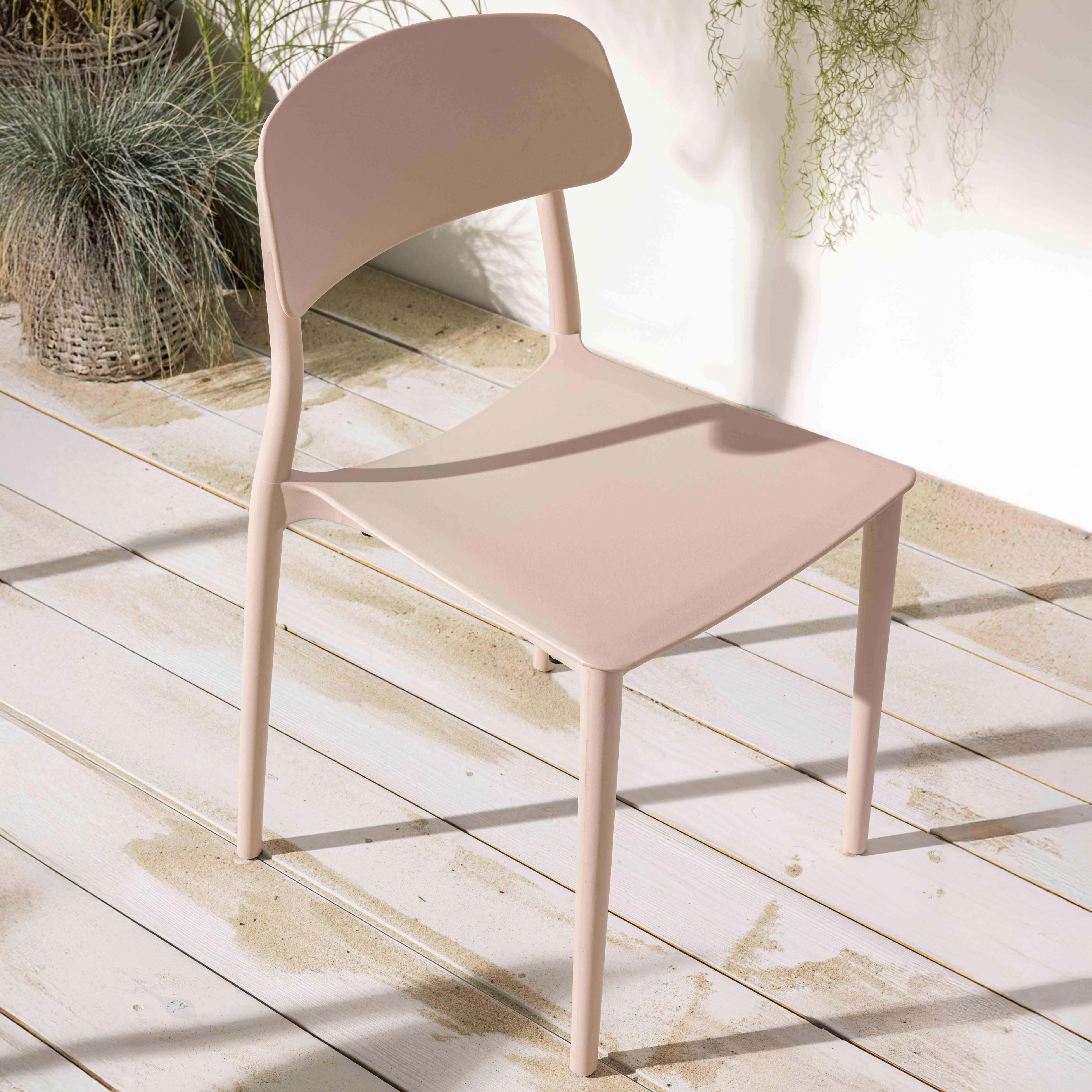Ein rosa Kunststoffstuhl steht auf einem Holzdeck, Pflanzen im Hintergrund, von Sonnenlicht durchflutet.