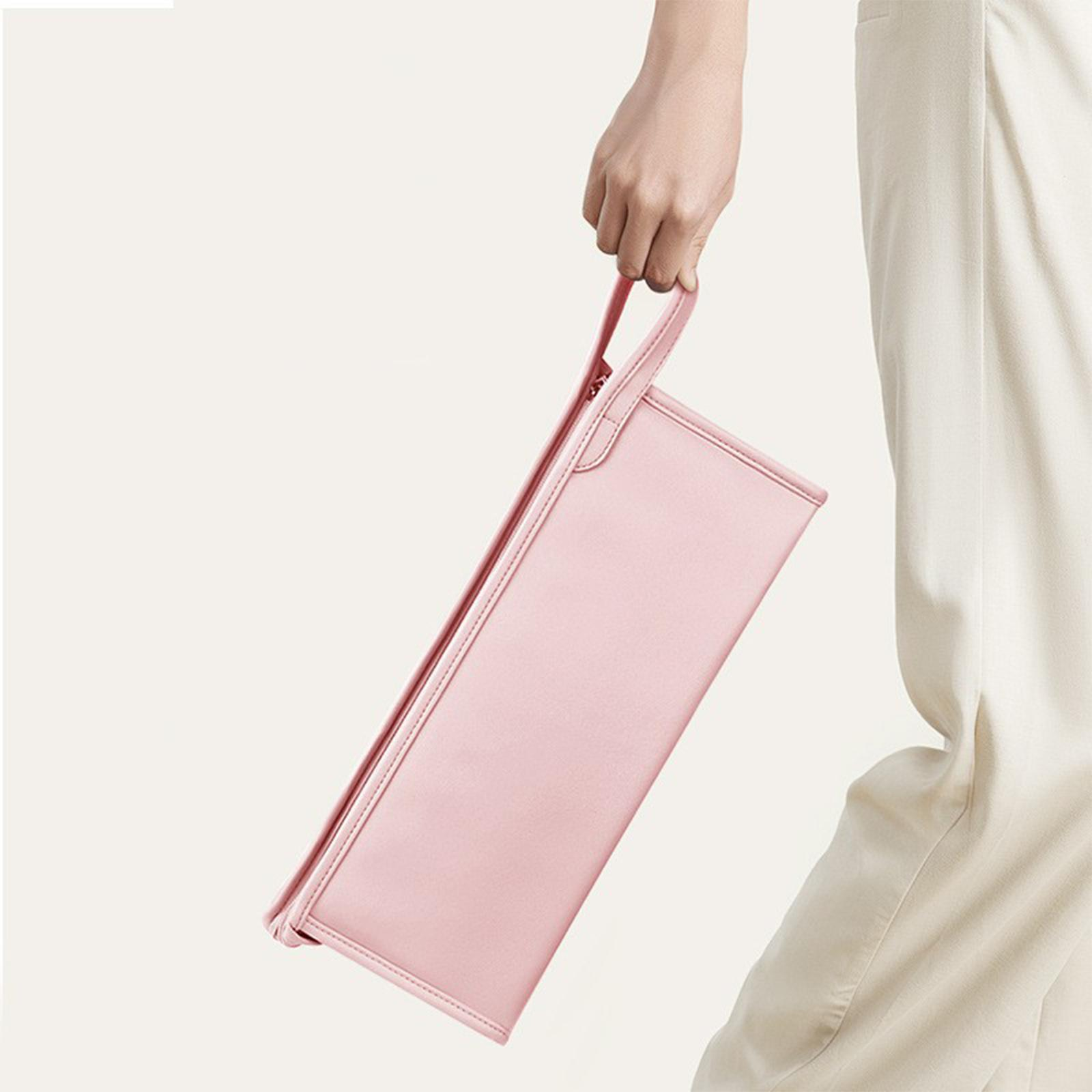 Eine Person hält eine rosa rechteckige Tasche mit Griff. Weiße Hose und Hintergrund.