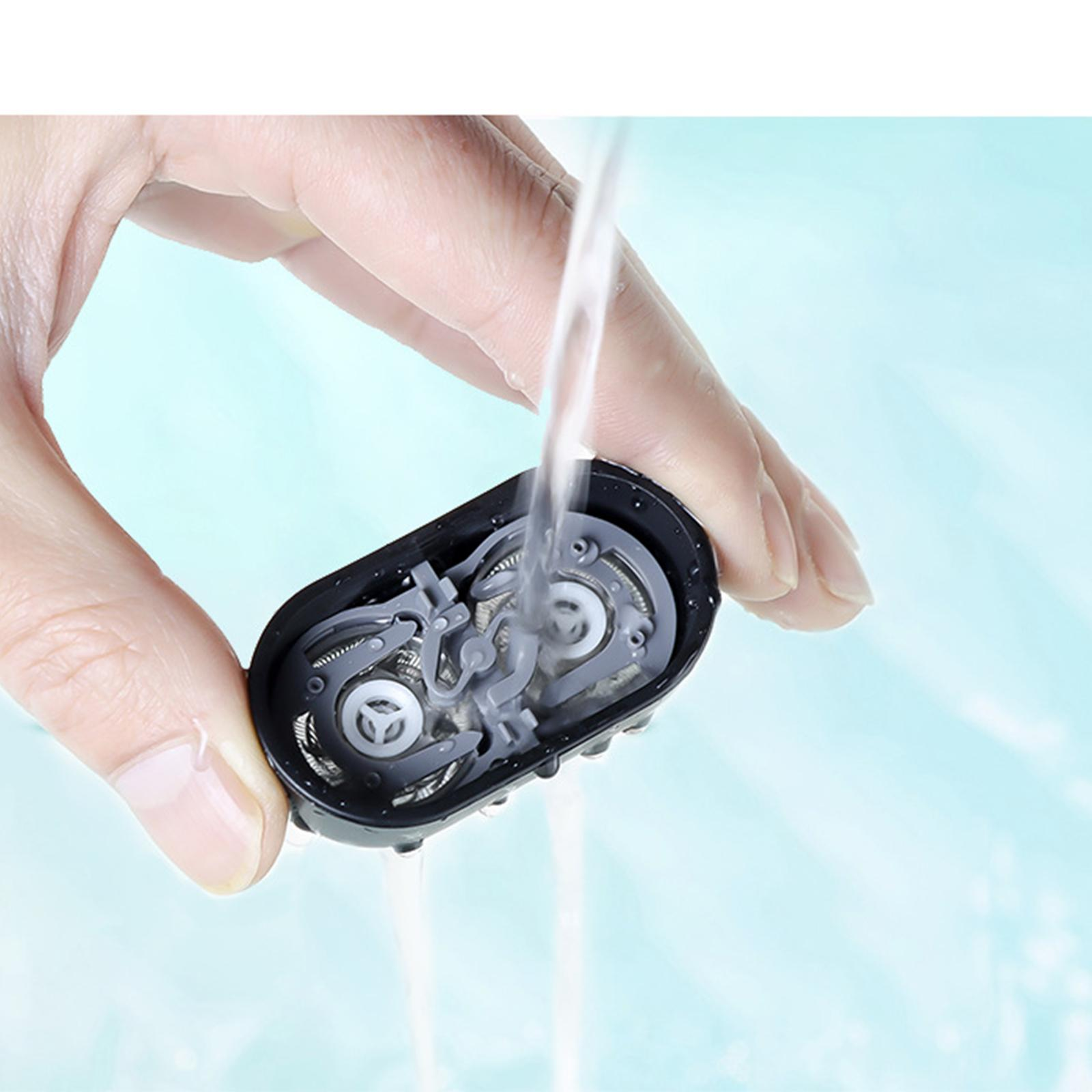 Eine Hand hält einen schwarzen Elektrorasierer unter fließendem Wasser. Die Köpfe des Rasierers sind sichtbar.