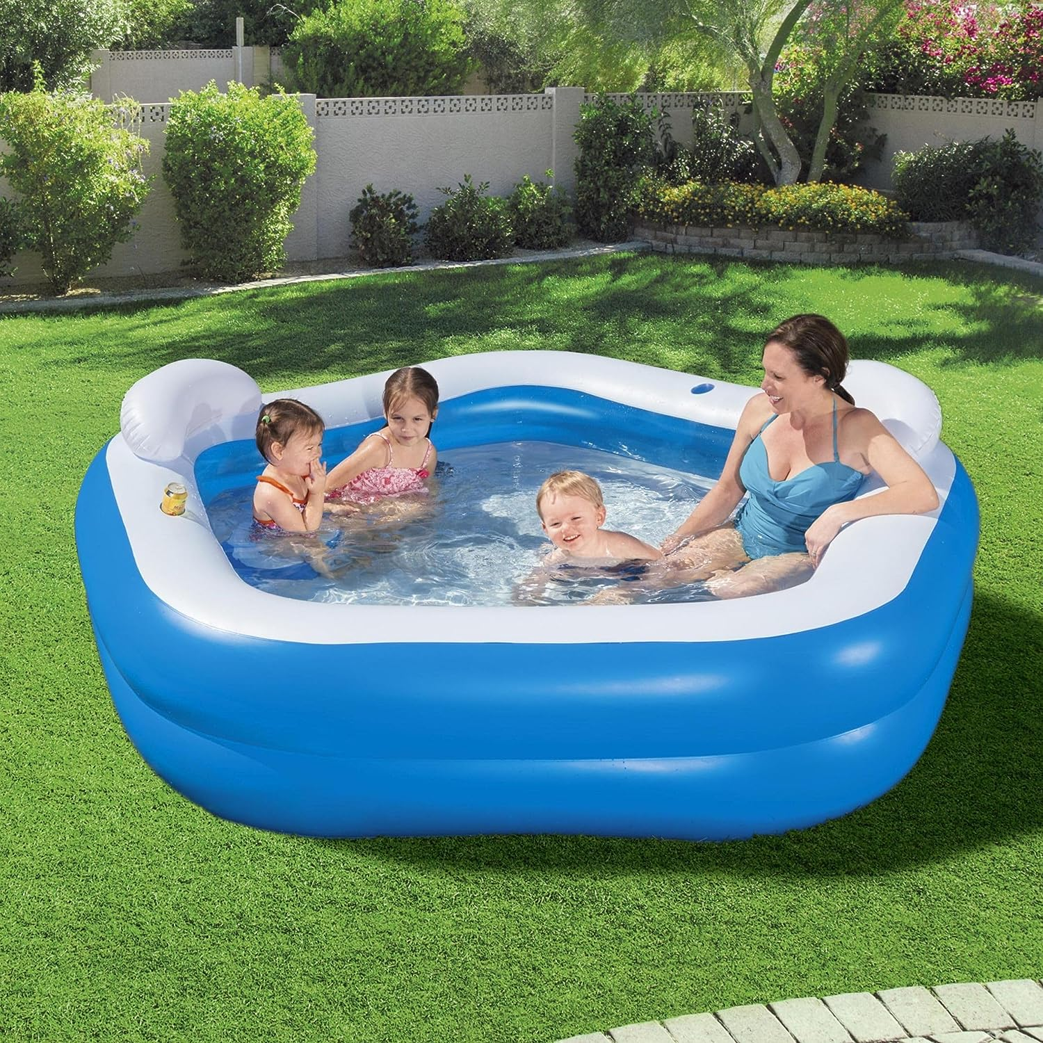 Familie in einem blau-weißen aufblasbaren Pool auf grünem Gras in sonniger Umgebung.