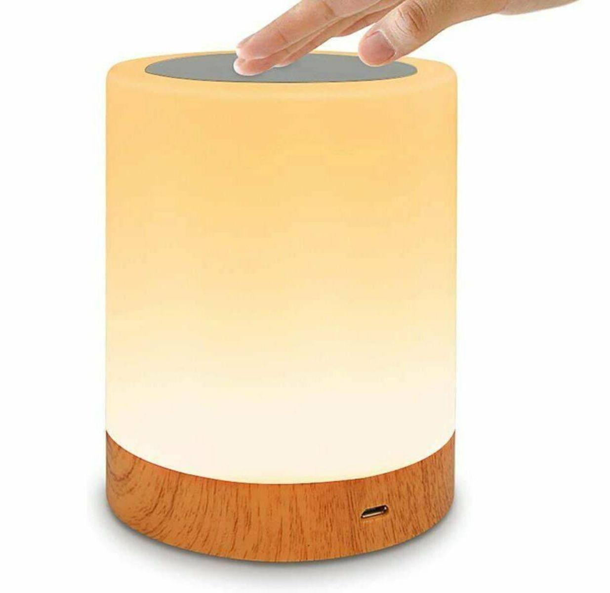 Eine Hand berührt die Oberseite einer Lampe, die ein warmes, weiches Licht ausstrahlt.