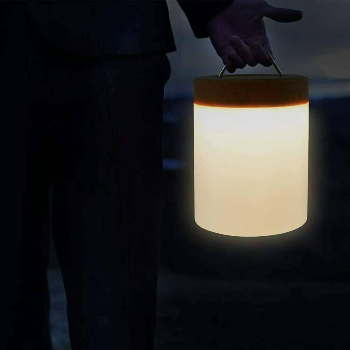 Eine Person hält eine leuchtende Lampe in einer dunklen Umgebung im Freien, mit einem Holzaufsatz.